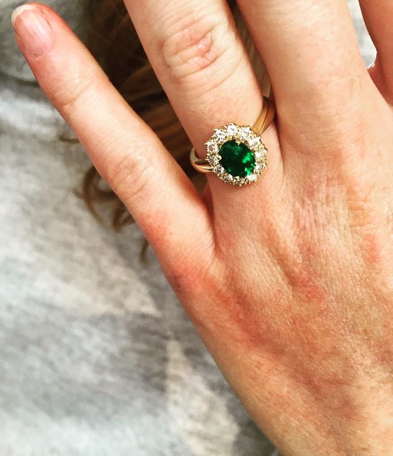 This is a 1.03 carat, oval cut deep, verdant green Colombian emerald, protected by over a carat of E-colour, VS2, round cut diamond points, set in 18 carat yellow gold to a bespoke design.