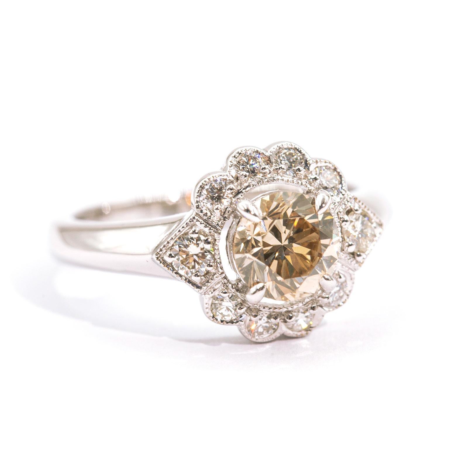 Forged in 18 carat white gold, this vintage inspired halo cluster ring features a high polish flat edge band with a sparkling centrepiece 1.03 carat ADGL certified round brilliant cut champagne diamond surrounded by a glittering border of shimmering