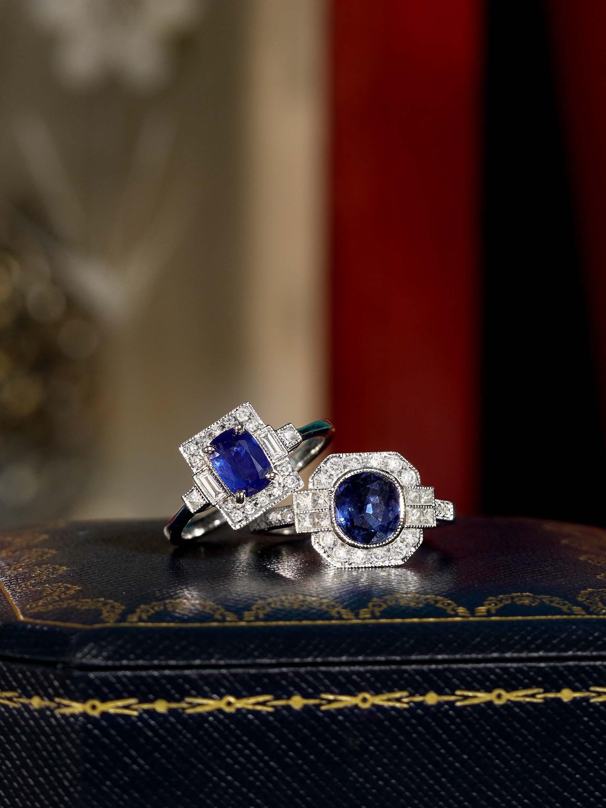 Un saphir bleu ovale de 1,03 carat, serti dans un carré, entouré d'un halo de baguettes et de ronds étincelants.  diamants. Les lignes épurées et le design géométrique évoquent le glamour vintage, tandis que l'association du saphir et des diamants
