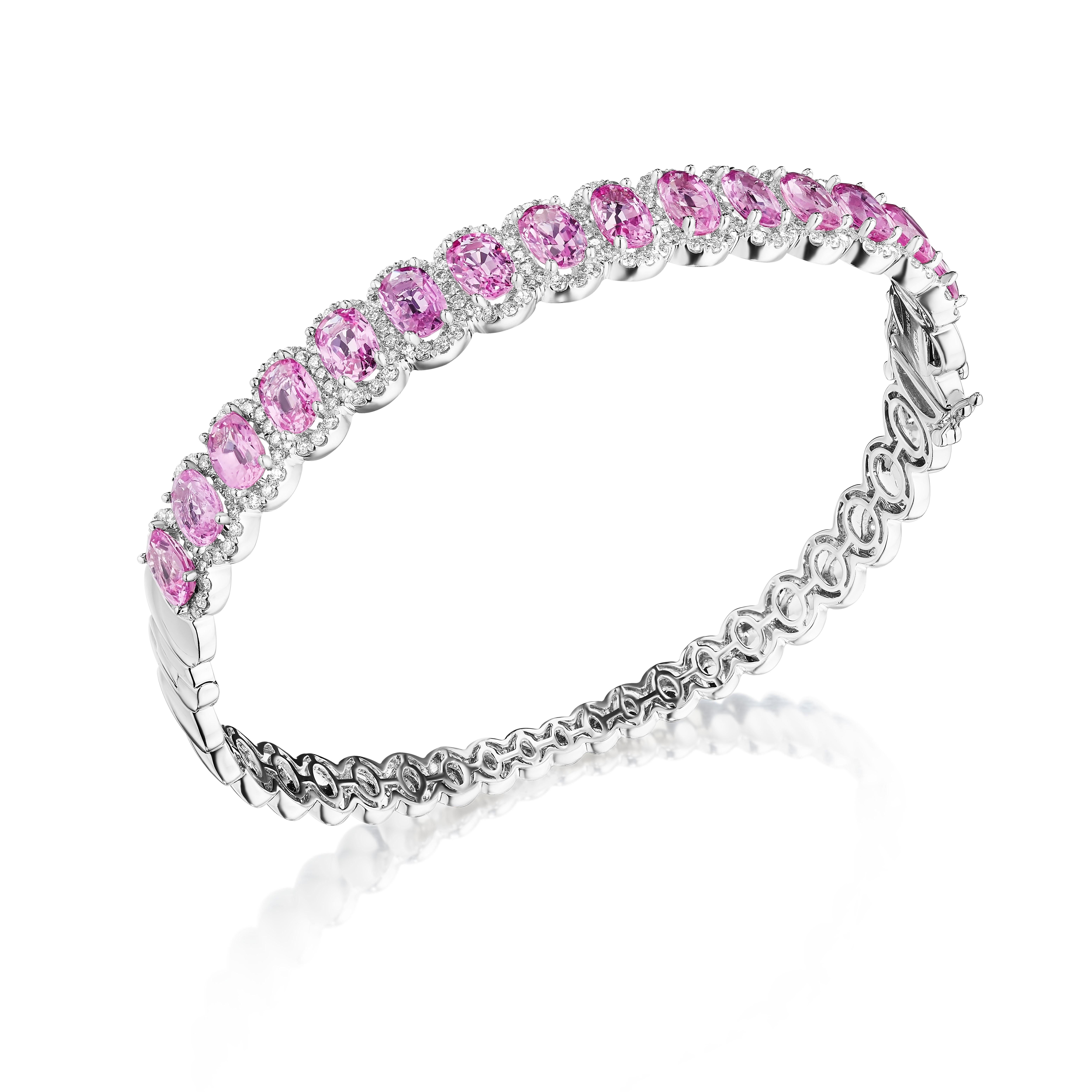 • A truly exquisite assortment of 15 oval cut pink sapphires is framed by delicate halos made of round brilliant cut diamonds in this beautiful bangle. The stones are set in 14KT white gold and have a combining total weight of approximately 10.35