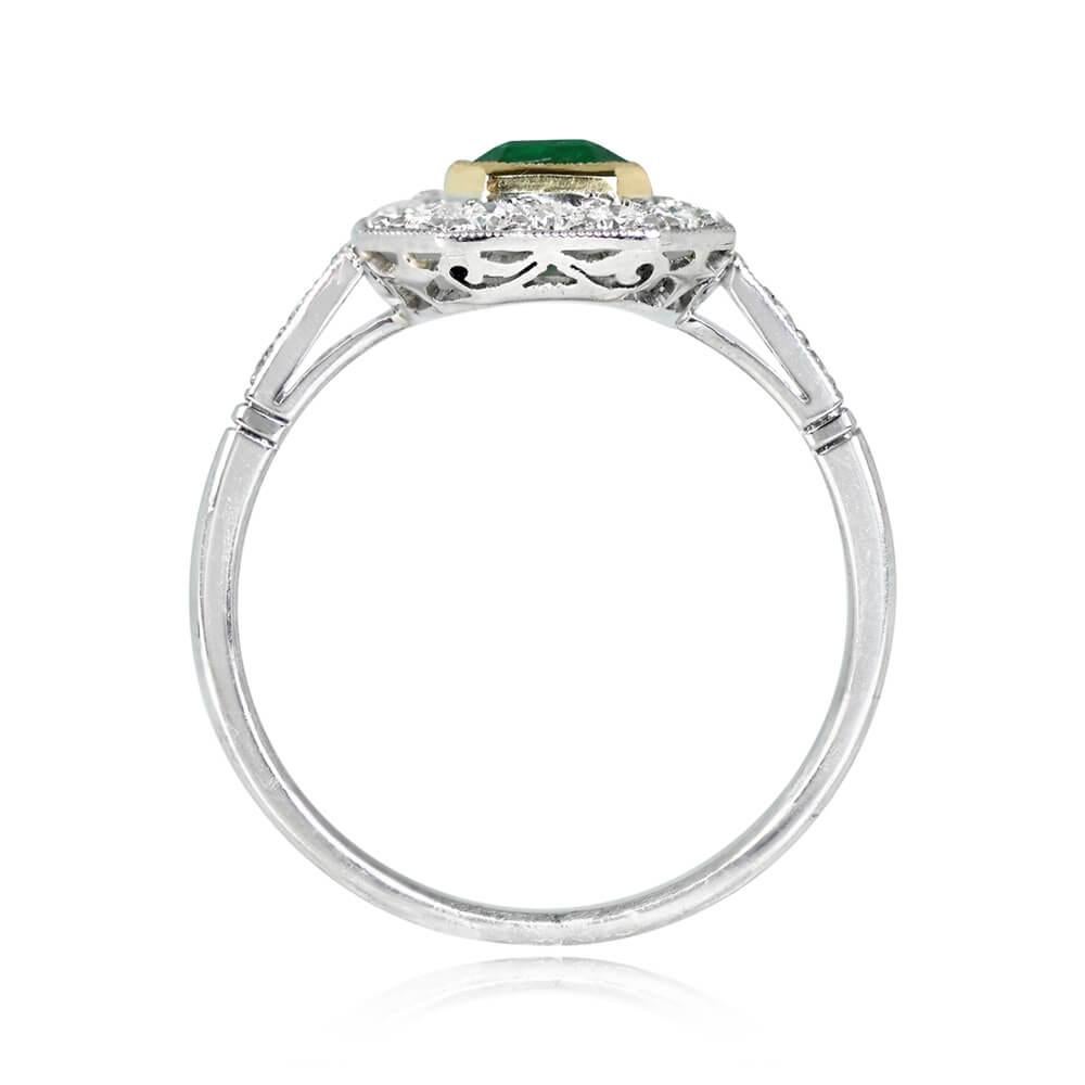 This engagement ring centers an emerald-cut emerald, bezel-set in yellow gold, and framed by a halo of old European cut diamonds. The center emerald weighs approximately 1.03 carats. The shoulders are set with an additional three diamonds each,