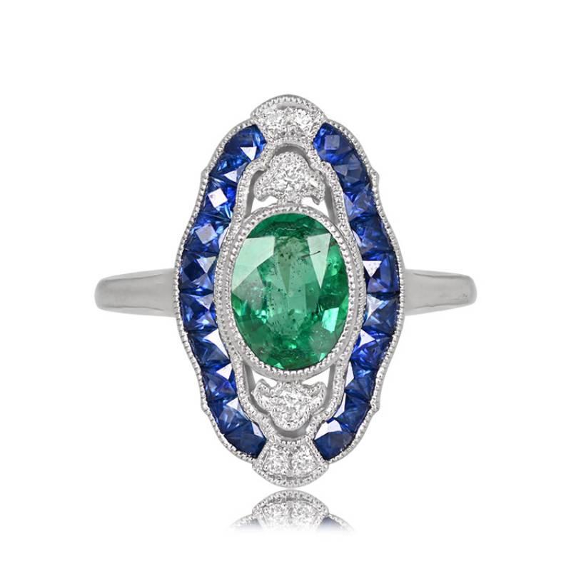 A captivating Egyptian revival ring boasts a 1.03-carat natural oval emerald as its centerpiece, encircled by approximately 0.20 carats of French-cut natural sapphires. Accentuating this unique piece are diamonds with a combined weight of around