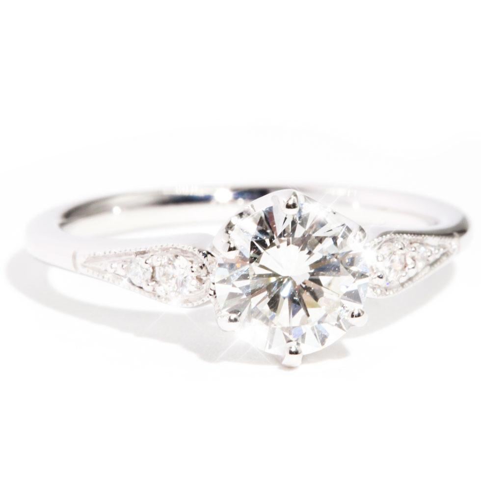 Carefully crafted in 18 carat white gold is this vintage inspired diamond ring featuring a sparkling 1.04 carat certified round brilliant cut diamond, and the band embellished with  six round brilliant cut diamonds gracefully flowing down the sides.