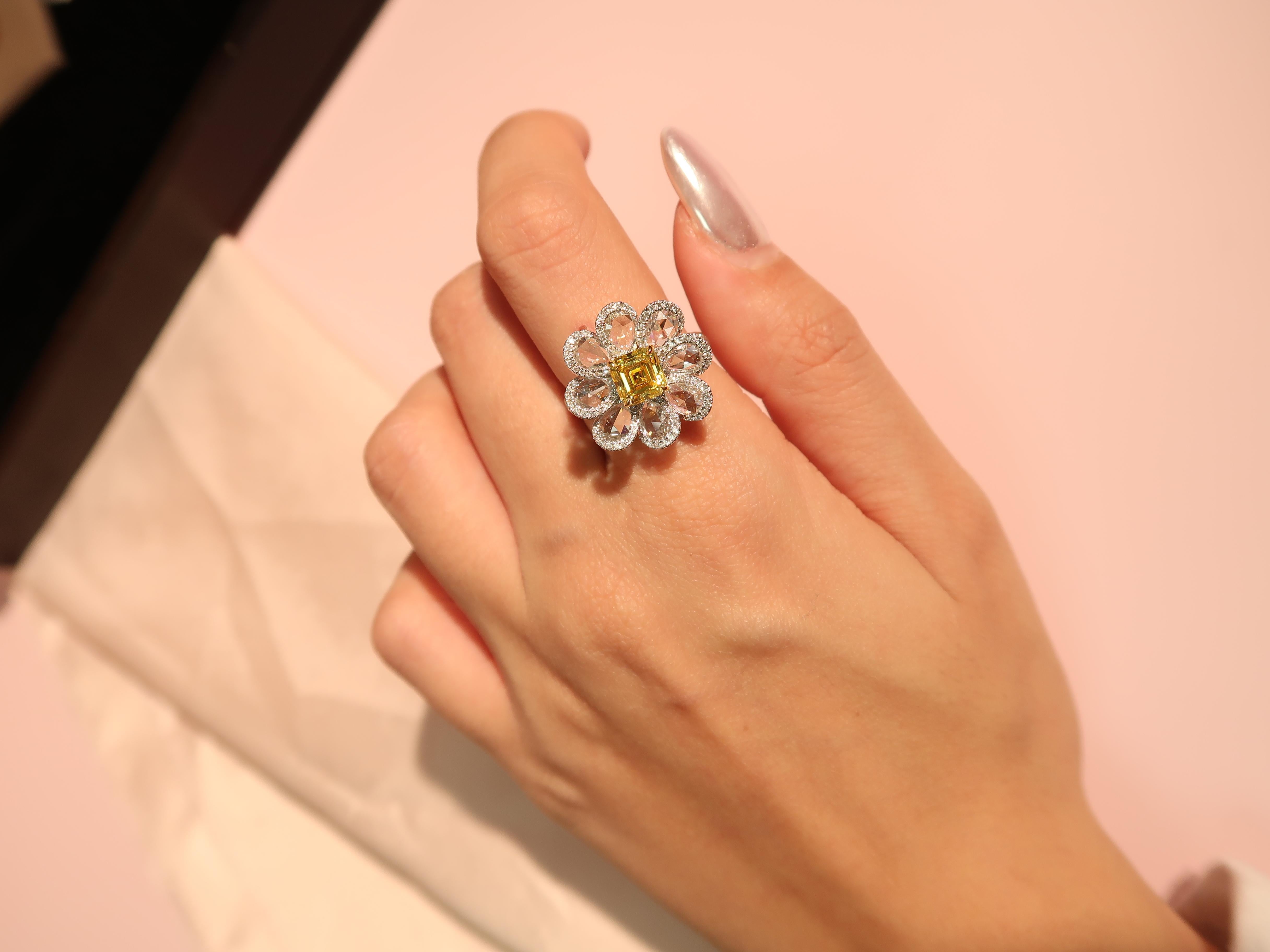 Ein wunderschöner Ring mit 1,04 Karat Fancy Vivid Yellow-Diamanten im Smaragdschliff, GIA-zertifiziert mit VVS2, eingefasst in ein charmantes Blumenmotiv. Der Ring besteht aus 8 birnenförmigen Diamanten mit einem Gewicht von 1,36 Karat, die von 116