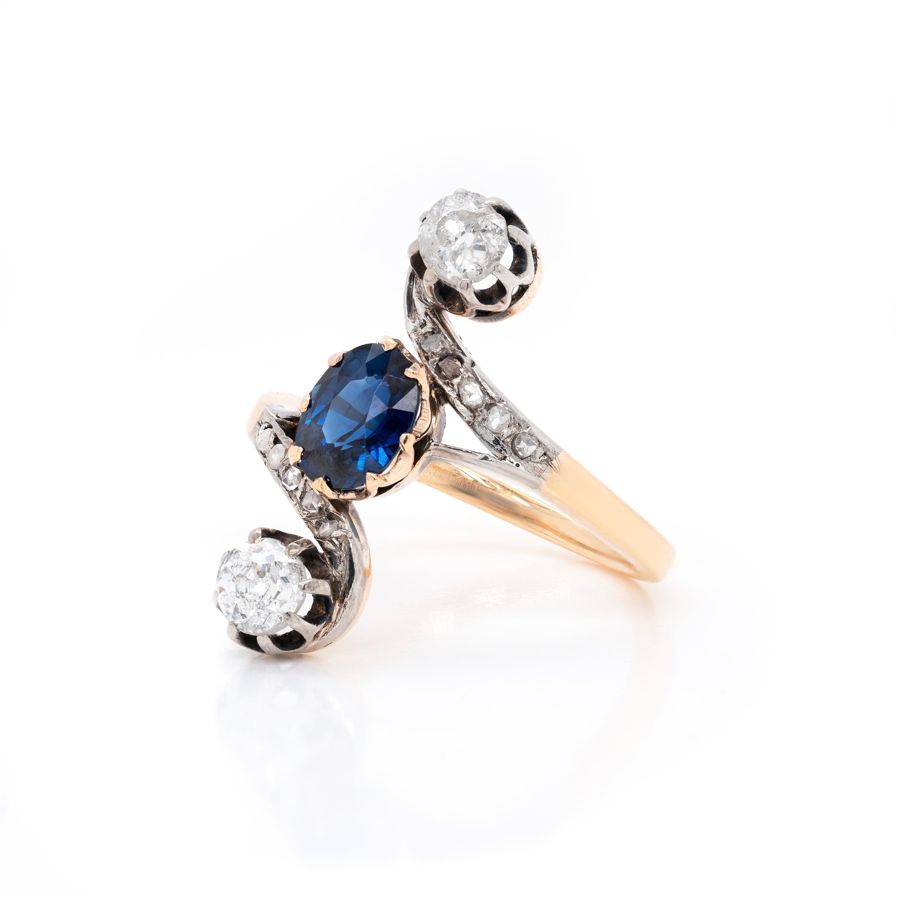 Late Victorian vertical three stone ring set with an oval blue sapphire weighing 1.04ct in an eight claw open back gold setting. The sapphire is beautifully accompanied by two old cut diamonds weighing approximately 0.25ct each, both in eight claw