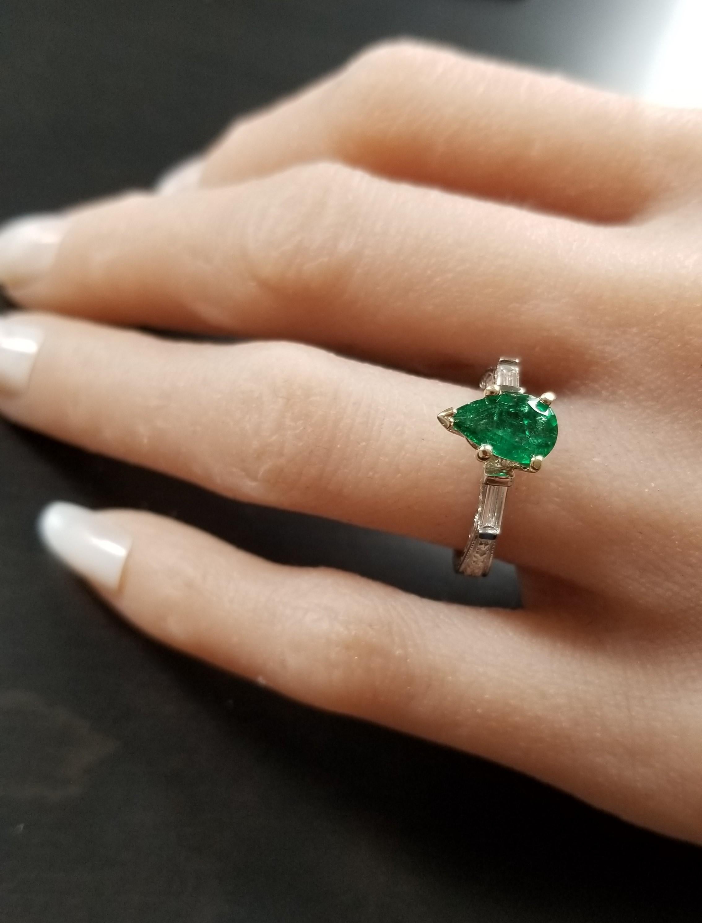An expertly cut 1.04 carat pear shaped green emerald takes center stage on this classic engagement/anniversary ring. Perfectly matched baguette cut diamonds adorn the sides in a channel bar setting. The hand engraving on the shank is exceptional.