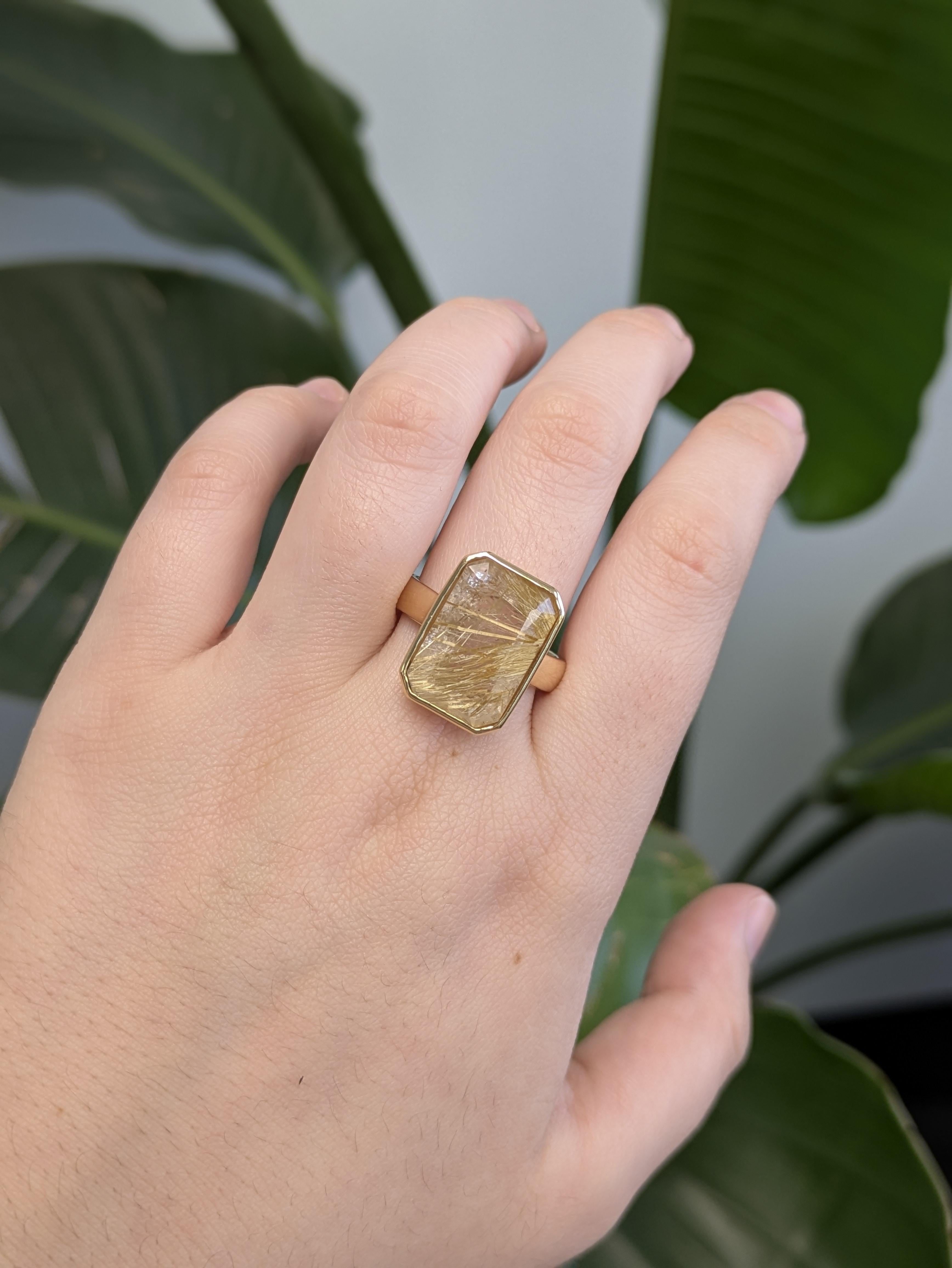 Élevez votre style avec cette bague en quartz rutilé de taille émeraude, sertie en or jaune 18 carats massif. Les aiguilles dorées uniques à l'intérieur du quartz captent magnifiquement la lumière, tandis que la lunette élégante offre une