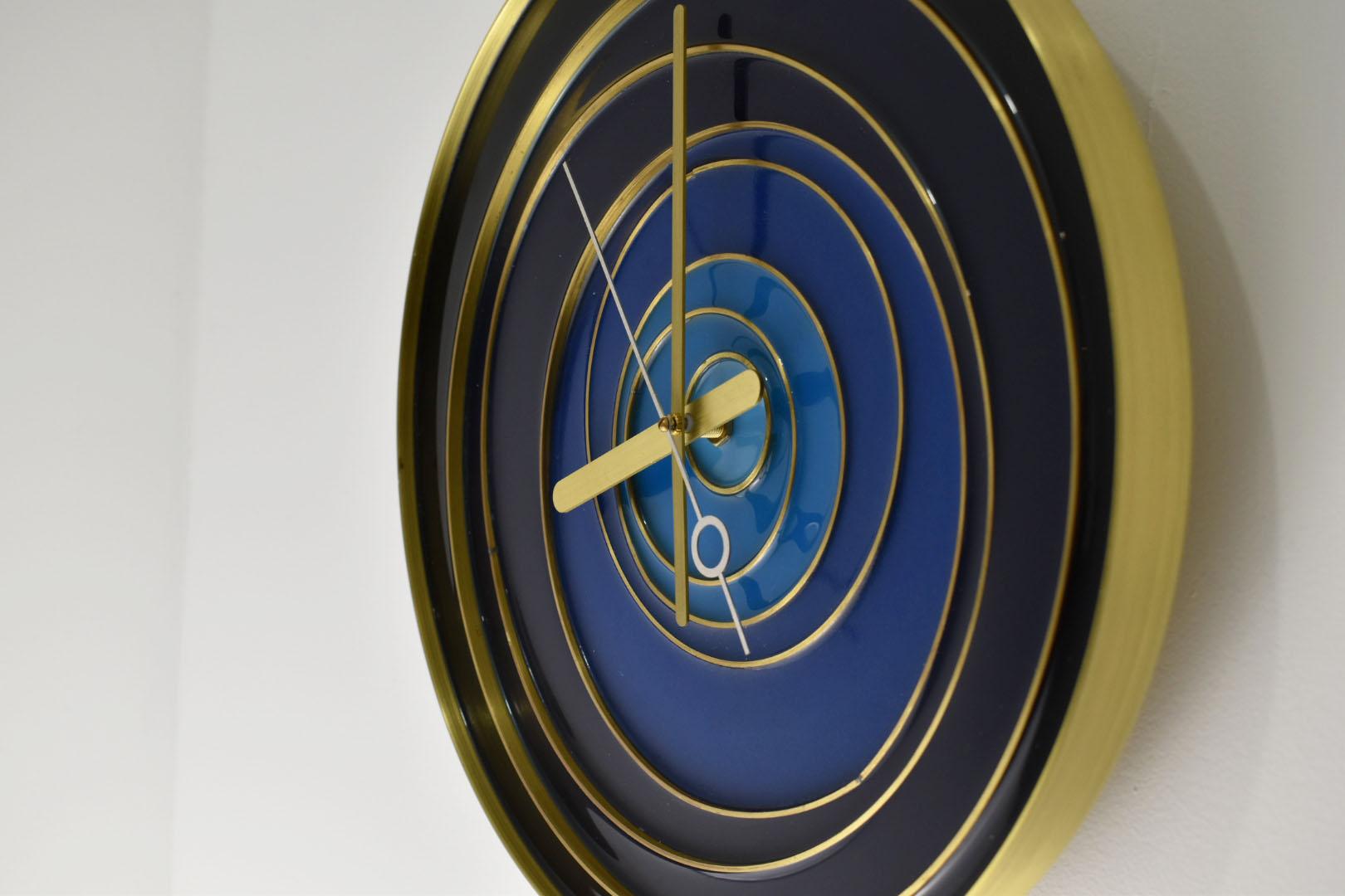 Diese atemberaubende Uhr ist aus einem einzigen gedrehten Stück massiven Messings gefertigt.  Sie ist  mit eingelegten Messingringen unterschiedlicher Größe gestaltet und anschließend mit getöntem Epoxidharz ausgegossen.   Die Stunden- und