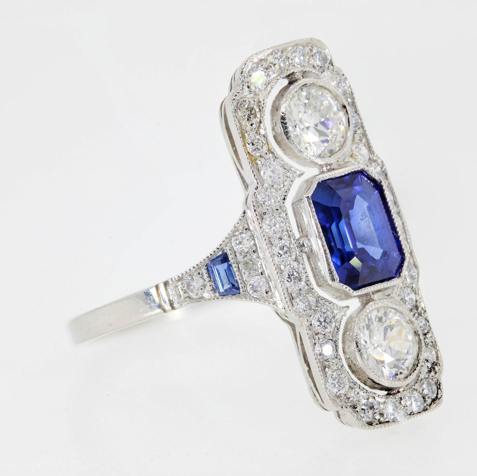 A hand crafted Art Deco style platinum that evokes the 1920s with its North/South design.  The 1.05 carats bright royal blue Ceylon Sapphire is flanked by two old cut natural diamonds.  All three bezel set stones are flanked by thirty Round