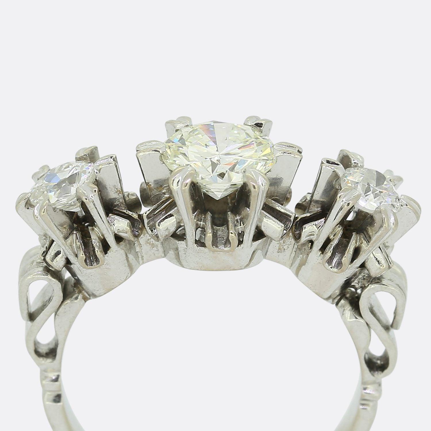 This is a vintage 18ct white gold three stone diamond ring. The central stone is a 0.75 carat round brilliant cut diamond which is closely flanked on either side by a single slightly smaller old cut diamond. Each stone here is claw set and very well