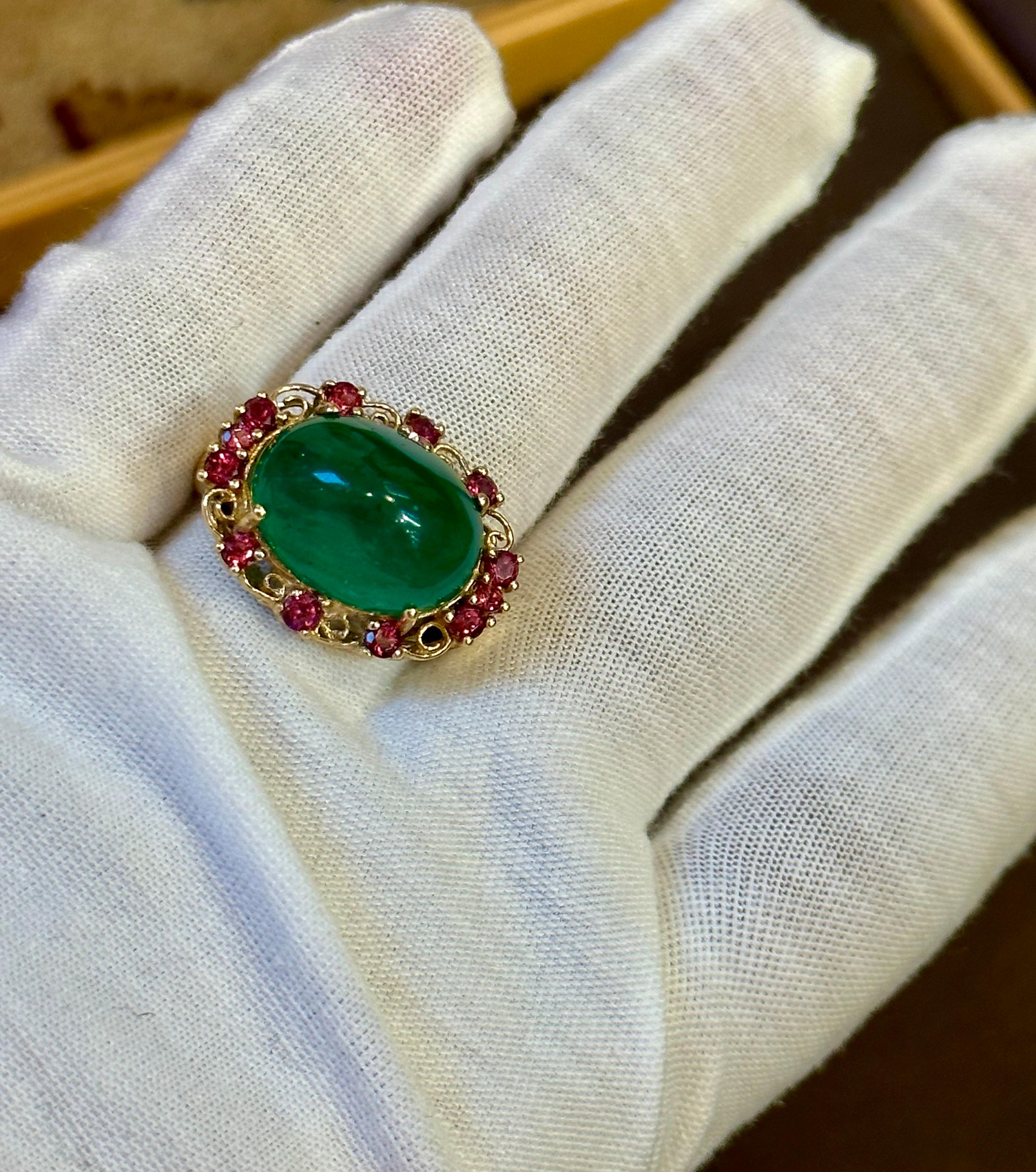 This classic cocktail ring features a stunning oval natural emerald cabochon surrounded by rhodolite garnet. The emerald is 10.5 carats and is estate with no color enhancement. The ring is crafted from 14 karat yellow gold and is stamped for