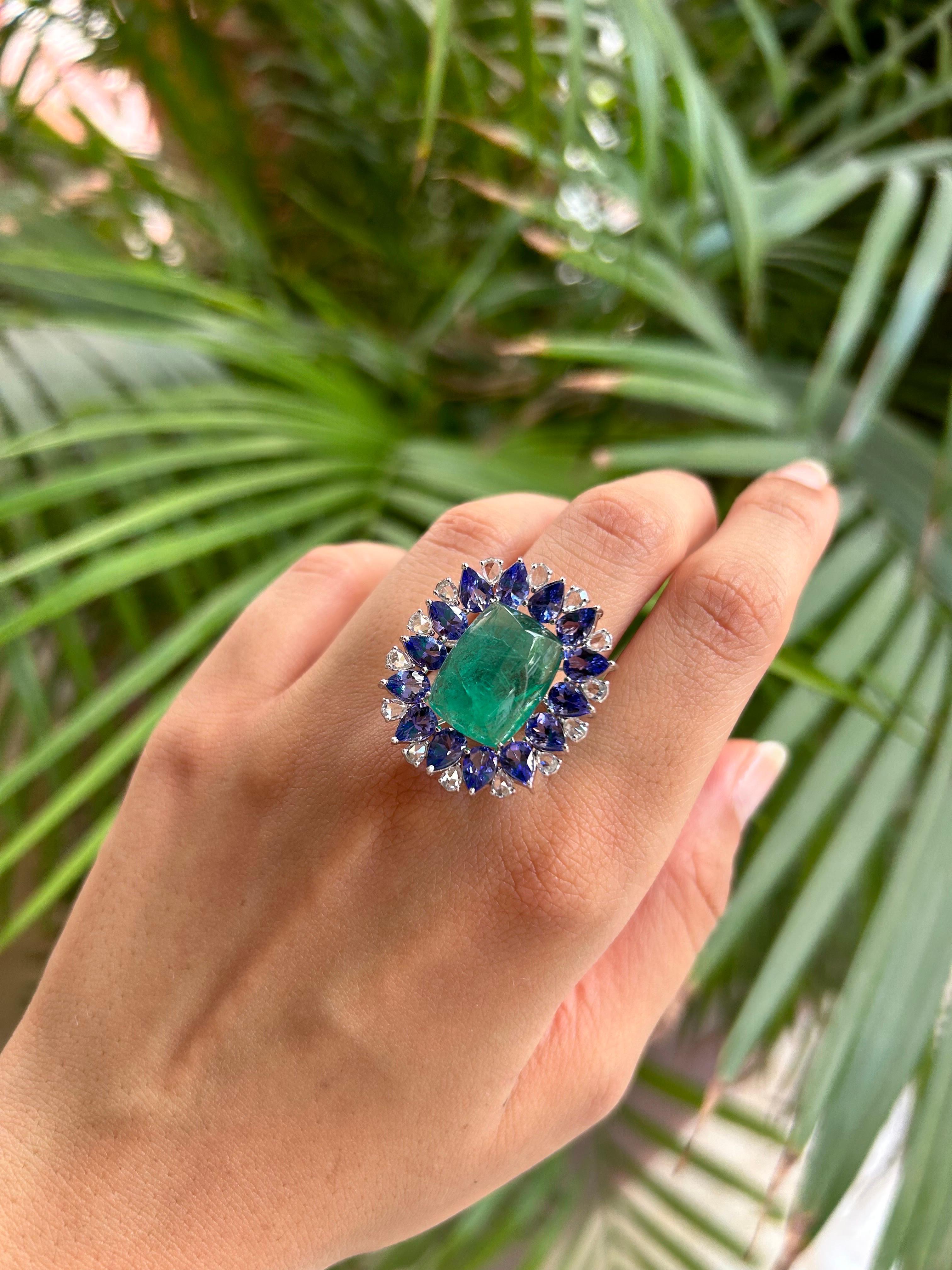 A beautiful 10.53 carat sugarloaf shaped natural Zambian Emerald cocktail ring, with 6.62 carat pear shaped Tanzanites surrounding it. The ring has 0.97 carats white diamonds, and is made in solid 18K White Gold. The ring is currently sized at US 7,