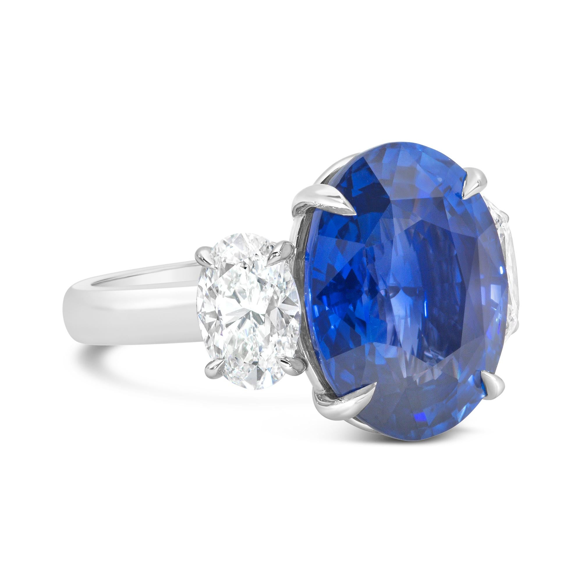 A brilliant engagement ring, featuring a 10.58 carats oval cut blue sapphire certified by C. Dunaigre as Ceylon/Sri Lankan origin, set with a timeless four prong setting. Flanked by two oval cut diamonds weighing 2.03 carats total. Elegantly made
