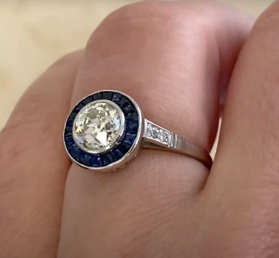 This exquisite halo engagement ring showcases a bezel-set old European cut diamond, weighing approx. 1.00-carats with a K color and SI1 clarity. The center stone radiates timeless elegance, accentuated by a meticulously crafted halo of French-cut
