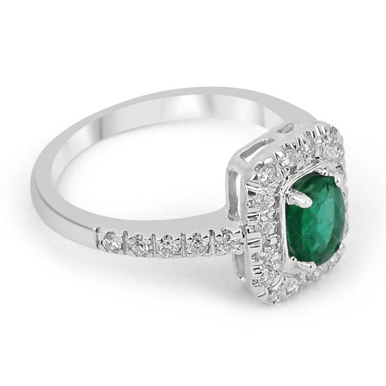 A stunning oval emerald and diamond halo hand-crafted engagement ring. The center stone features a lovely 0.70-carat, natural earth-mined emerald with a vivid dark green color and excellent luster. Surrounding the center gemstone are multiple