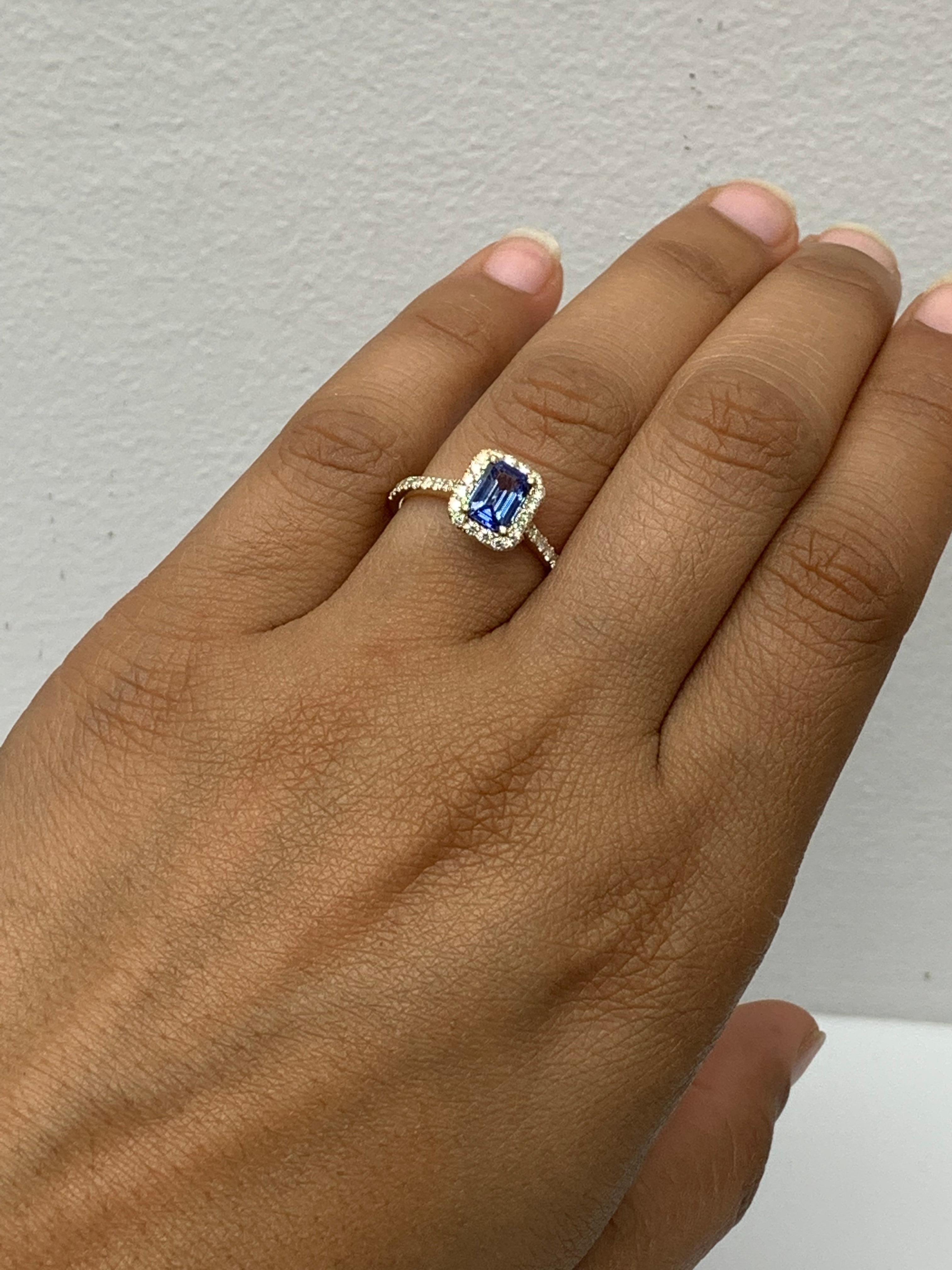 Showcases an emerald-cut blue sapphire weighing 1.06 carats, surrounded by a single row of 36 round brilliant diamonds in a seamless halo design. Set in a thin 14-karat yellow gold band accented with diamonds. Diamonds weigh 0.49 carats in