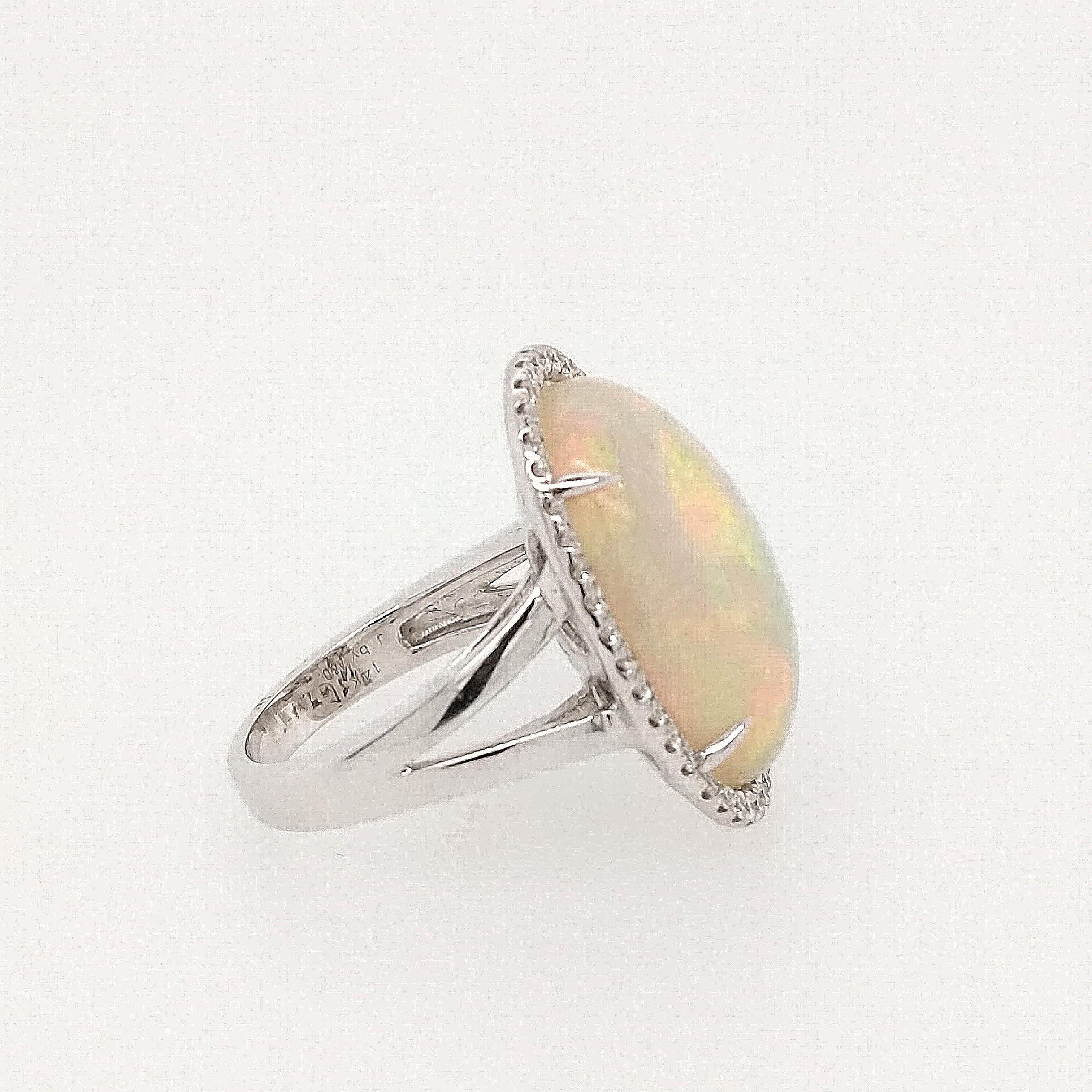 This Opal and diamond ring is crafted in 14k white gold and features (1) cabochon opal weighing 10.77ct with dominant colors of green, orange, red, blue and white. The center stone is surrounded by (42) round brilliant diamonds weighing
