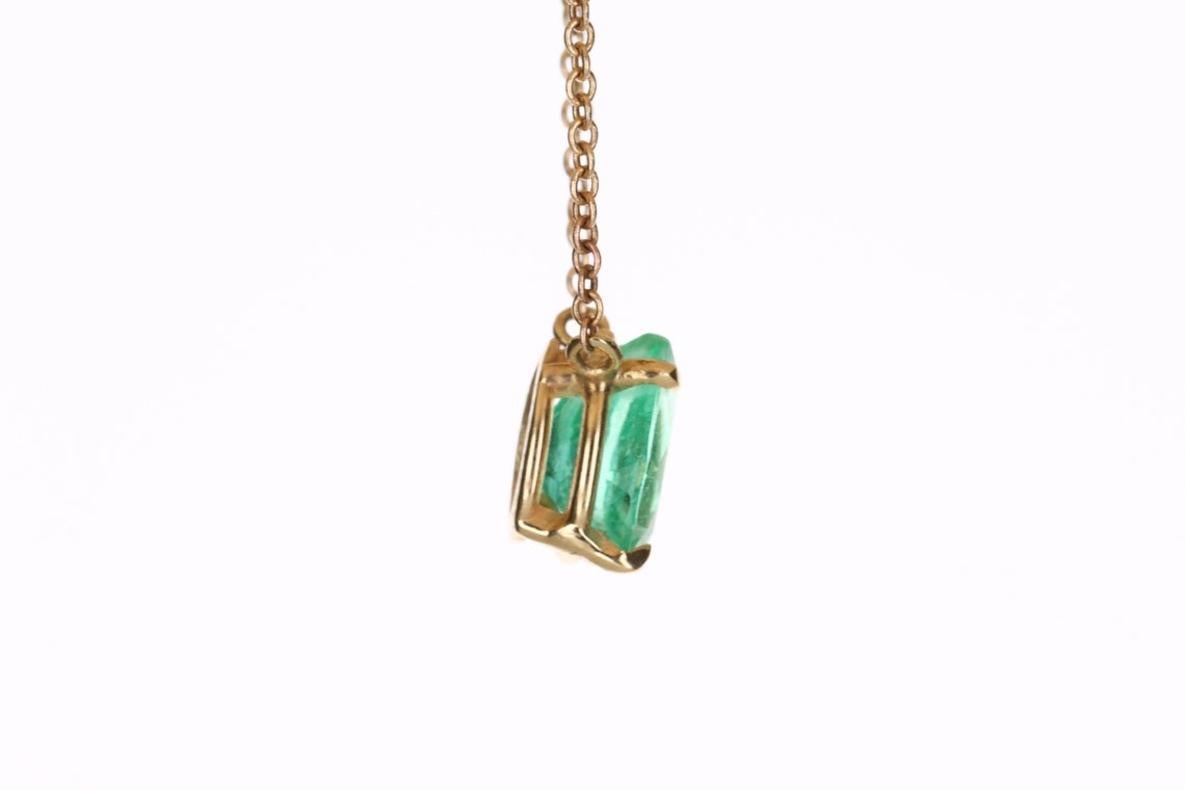 Displayed is a classic Colombian emerald solitaire necklace set in 14K yellow gold. This gorgeous solitaire piece carries a natural emerald in a four-prong setting. Fully faceted, this gemstone showcases excellent shine. The emerald has very good