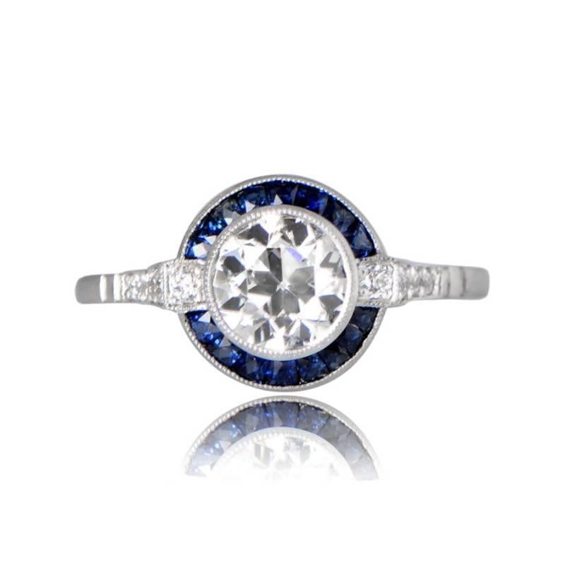 The Milan Ring showcases a captivating old European cut diamond at its center, encircled by a halo of French cut sapphires. The antique diamond is secured within a bezel adorned with intricate milgrain detailing. The ring's shoulders are adorned