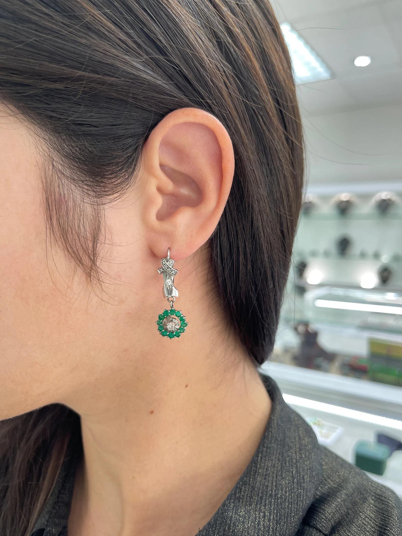 A stylish pair of unique emerald and diamond earrings. Showcasing an exquisite halo of all vivid dark green emeralds with stunning characteristics. Within the halo is a brilliant round-cut diamond and a few more accenting above the halo