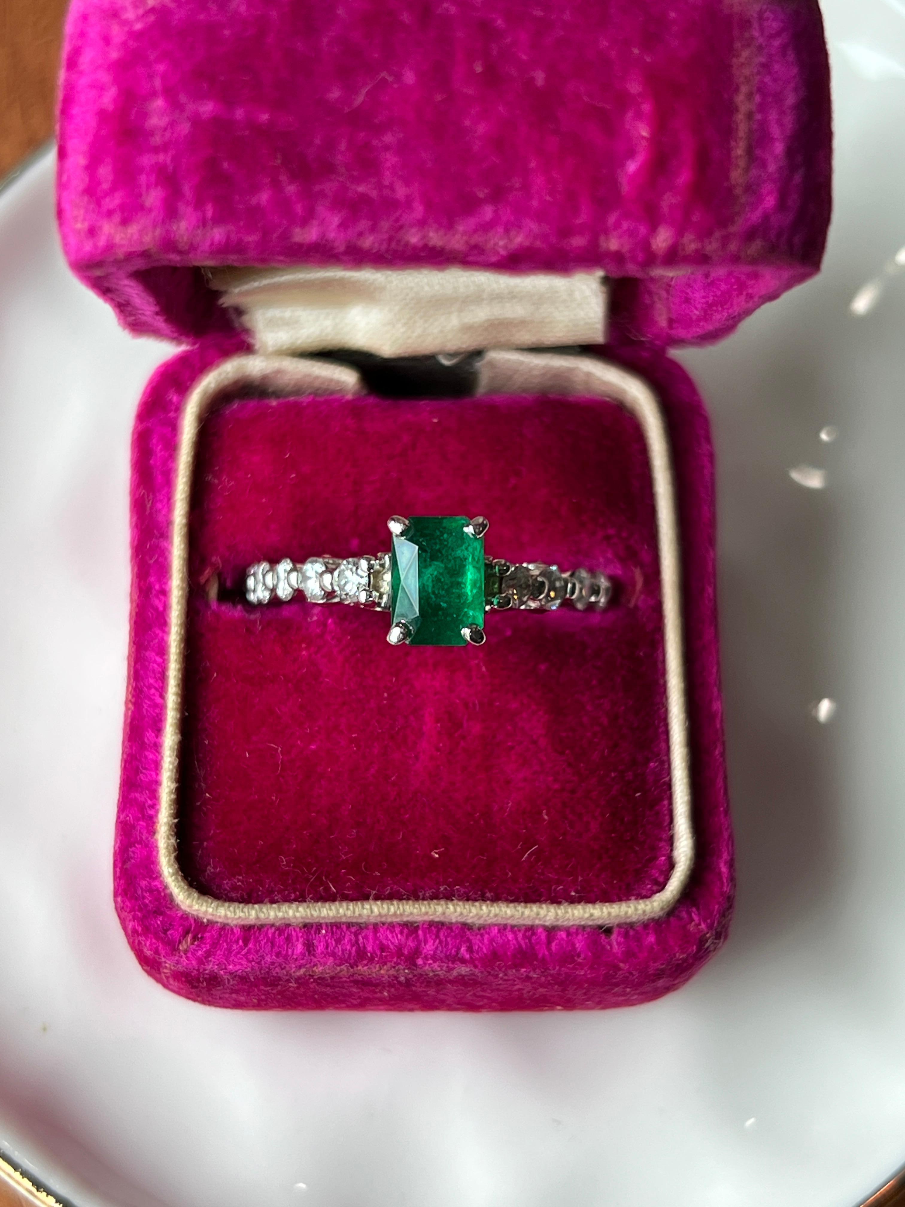 A contemporary 14 karat white gold ring centered with a striking emerald-cut emerald weighing approximately 1.08 carats. The rich green hue of the emerald is beautifully complemented by ten round brilliant diamonds, each approximately 2.5mm, for a
