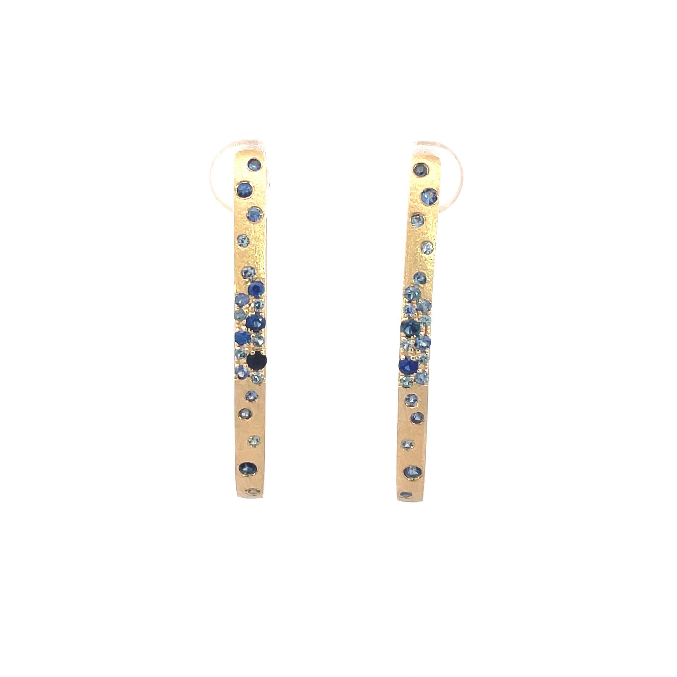 These Sapphire earrings are a stunning and timeless accessory that can add a touch of glamour and sophistication to any outfit. These Flush Set Oval Hoop Earrings contain 1.08 Carats of Round Light, Medium, and Bright Blue Sapphires , set in 14K