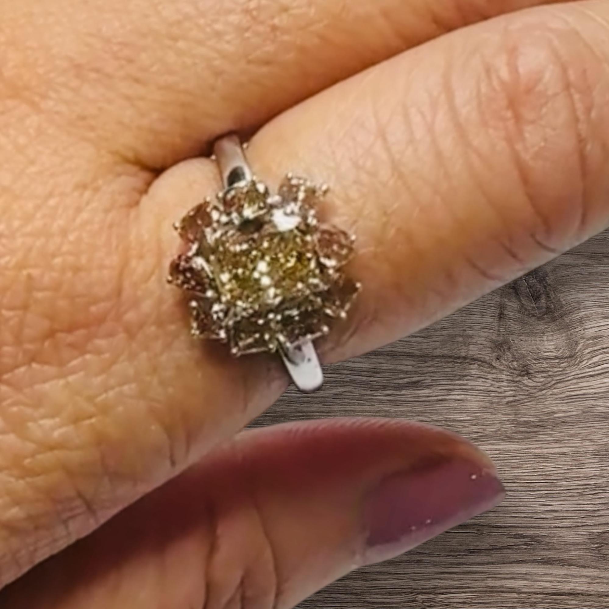 In der Mitte dieses Clusterrings sitzt ein 1,08ct Cushion Cut Fancy Brown Coloured Diamond, eingefasst in vier Krallen aus 18ct Gelbgold.  Der Mittelstein ist von vier oval geschliffenen Diamanten, drei Diamanten im Kissenschliff und einem Diamanten
