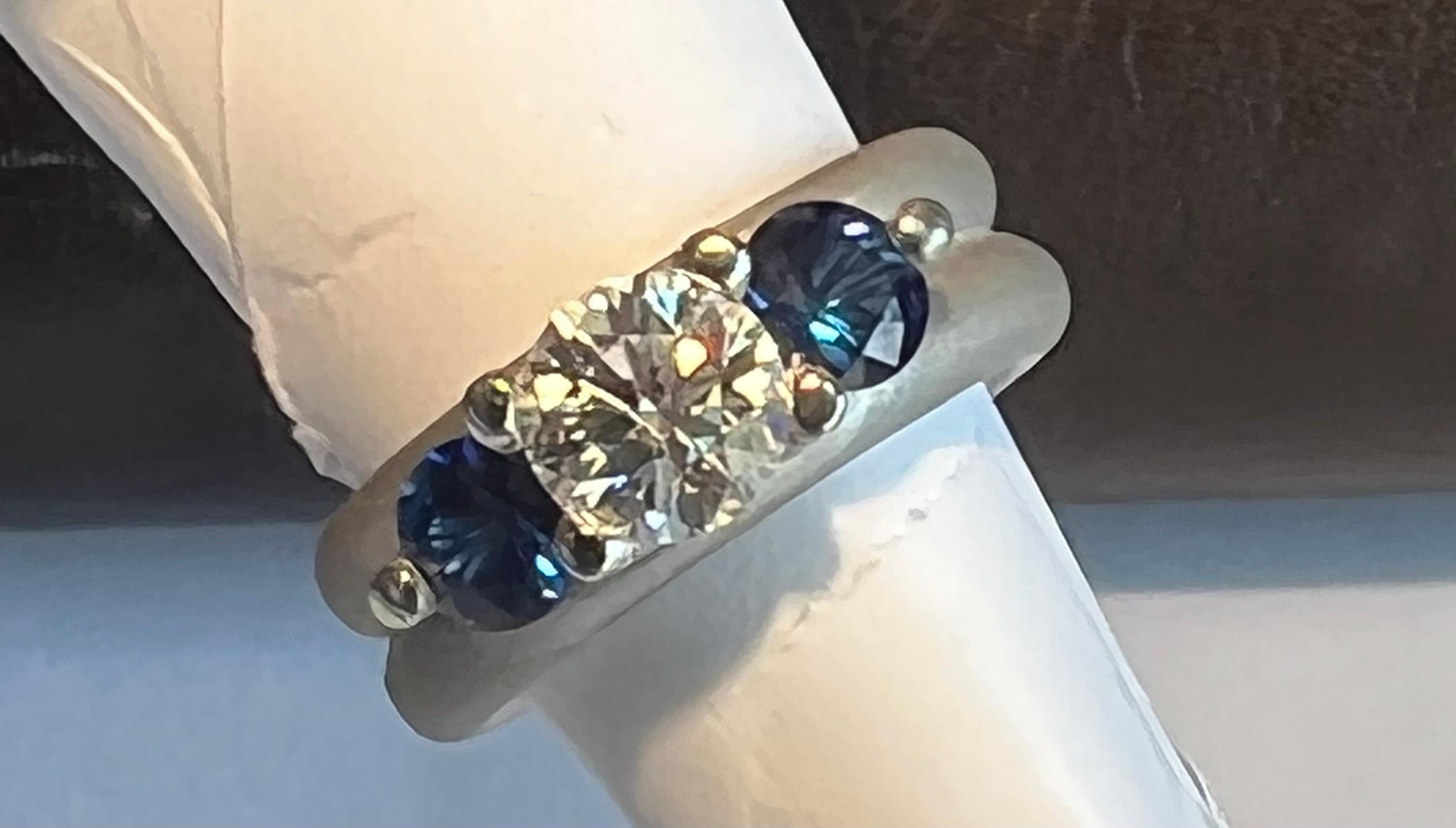 1.08ct round diamond, FG color, VS2 clarity prong set with two round blue sapphires weighing 1.22cts, in brushed satin finish platinum mounting, 7mm width, finger size 6, may be sized.
Original retail $10850