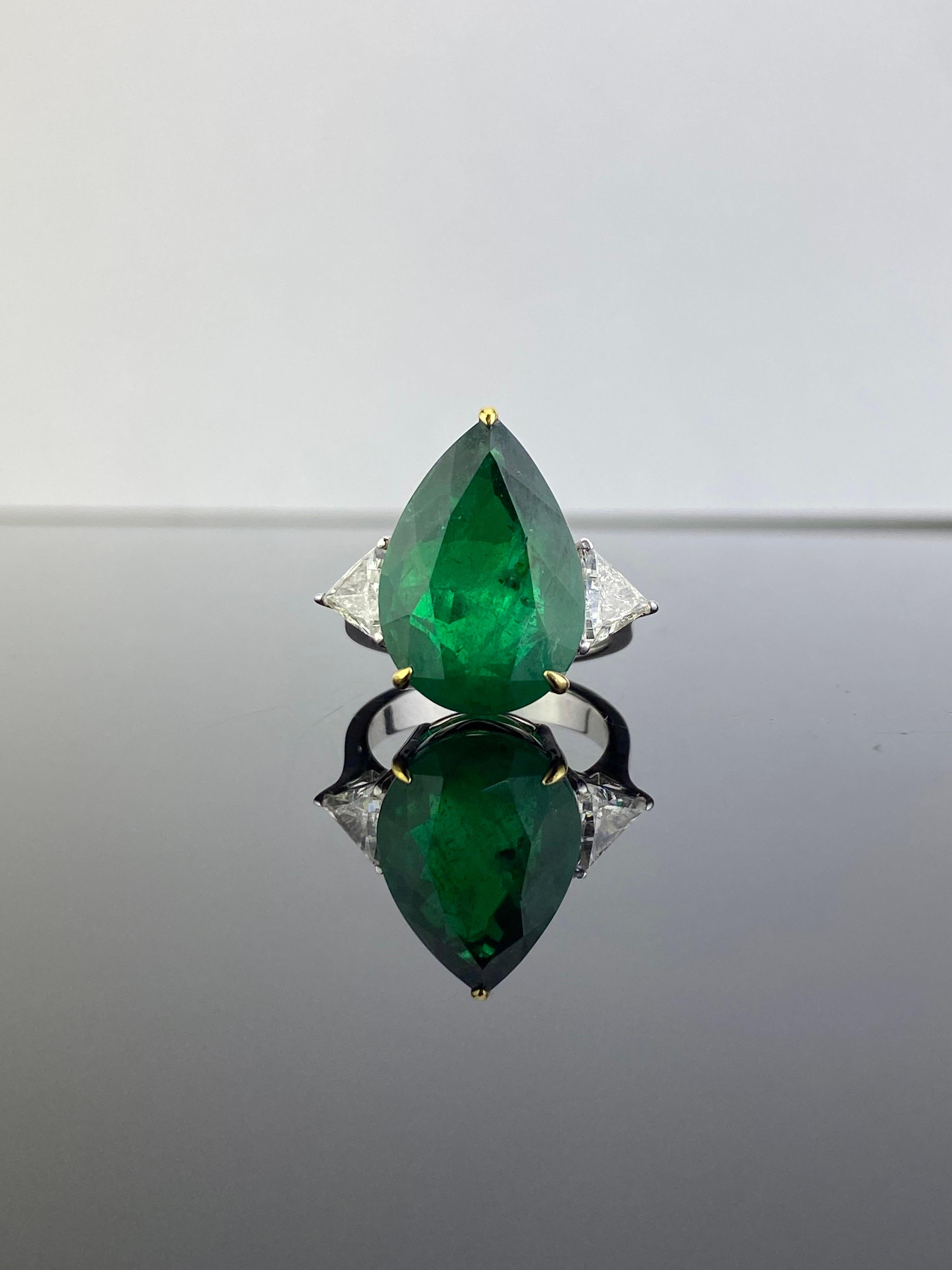 A gorgeous, Emerald and Diamond three-stone engagement ring. With a 10.97 carat pear shape Emerald in the centre, with 2 pieces 1.01 carat trillion shape White Diamonds on the side. The Emerald is of Zambian origin, with a beautiful vivid green