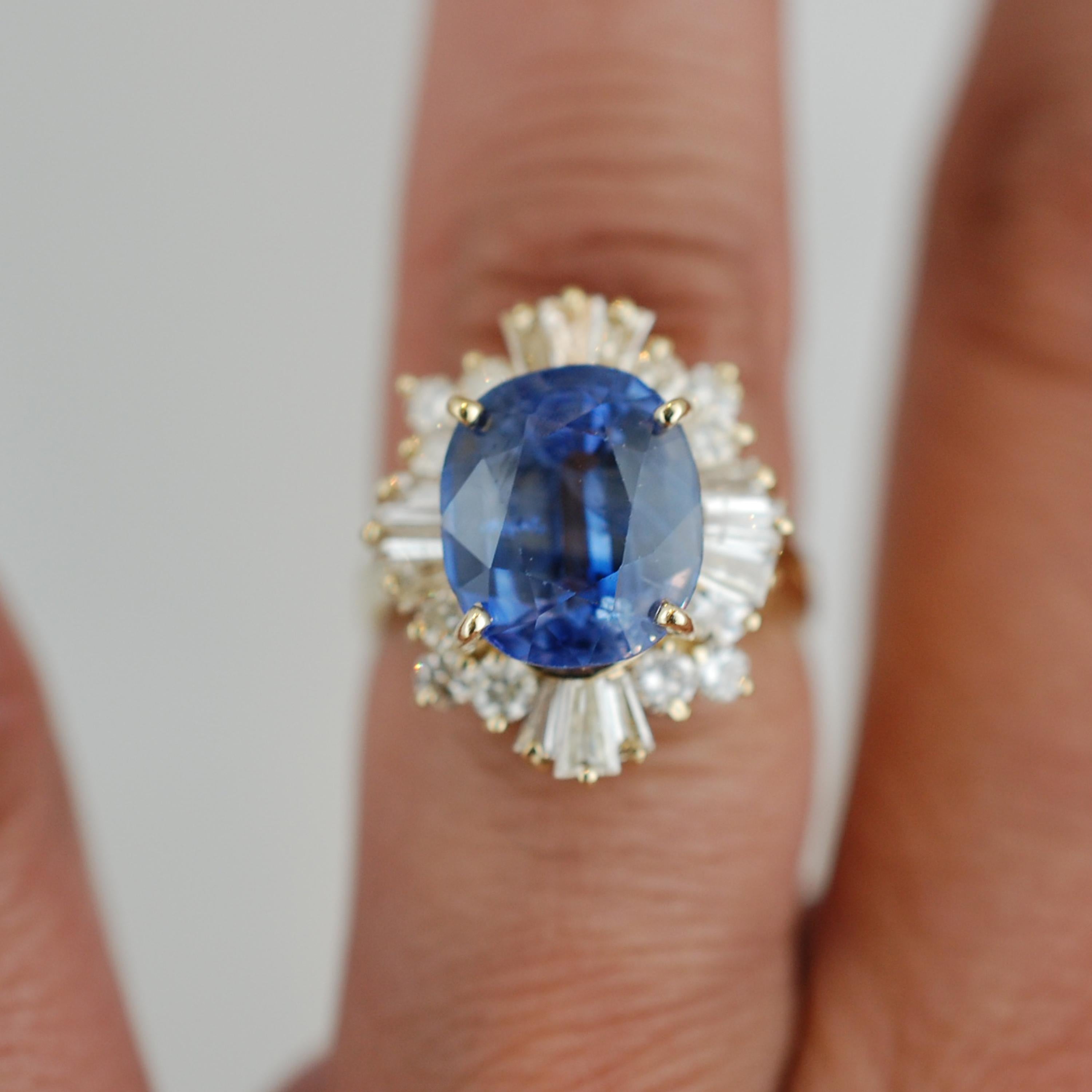 This sapphire and diamond ring contains the following.  One oval sapphire that has cornflower blue violet color and SI clarity with indications of no heat.  The sapphire measures 11.65 x 9.95 x 7.01 mm.  The center sapphire is surrounded by four 4