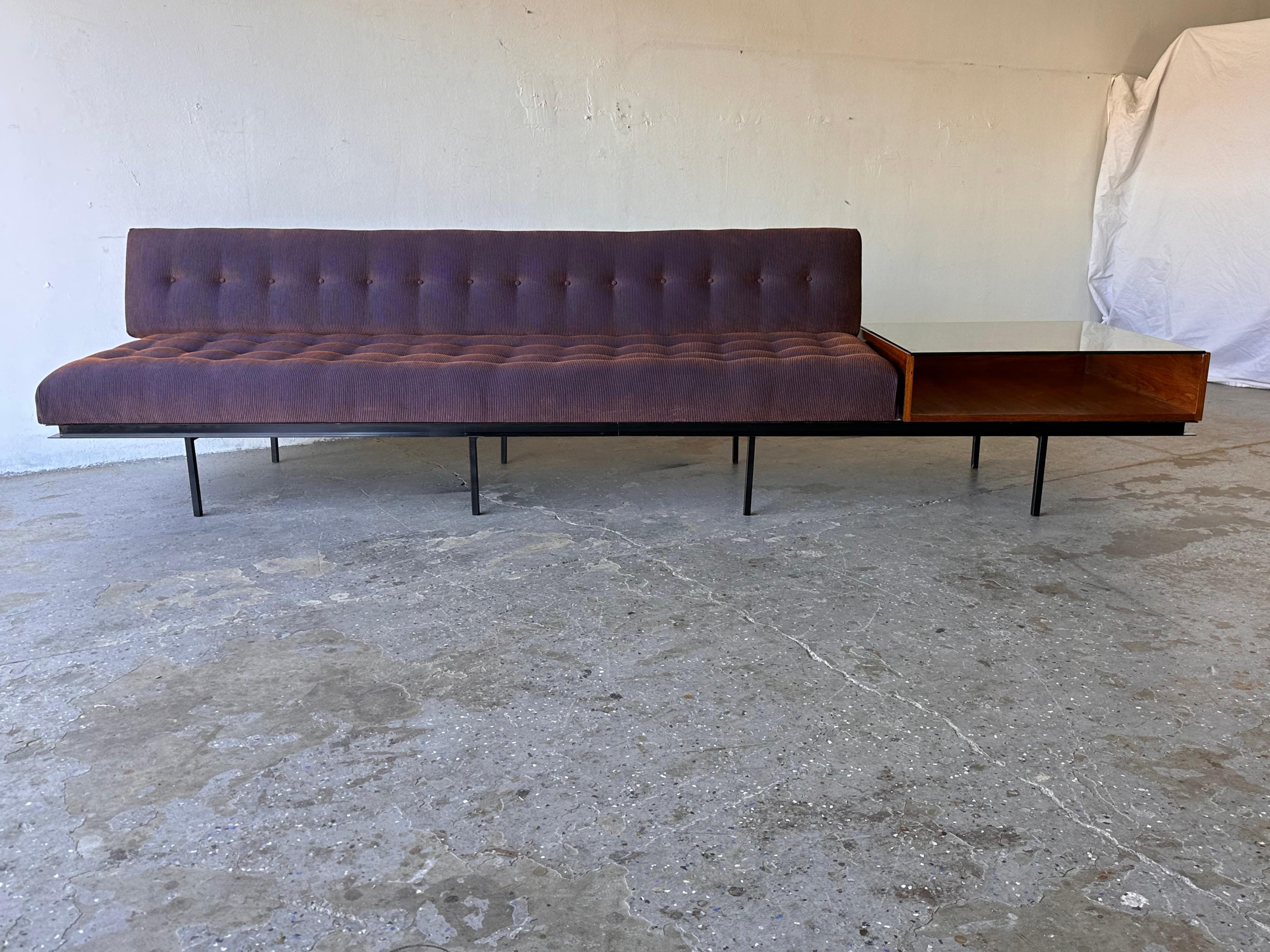 Authentic early sofa and end table designed by Florence Knoll in the mid 1950s. It features a  steel frame with eight square, tubular legs and an attached walnut table with glass top. The Iridescent fabric has shades of purple and is not  original..