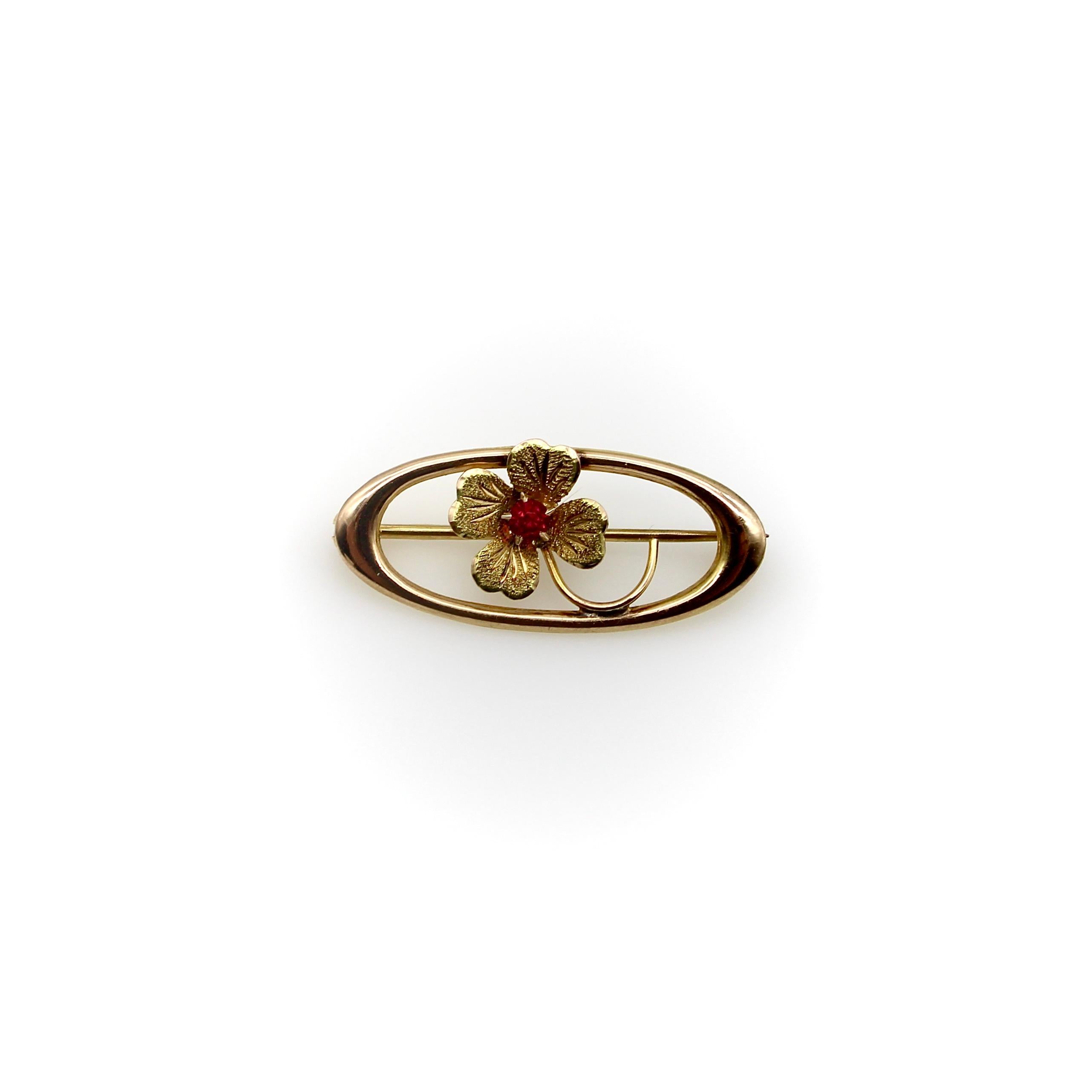 This adorable 10k gold pin brings a little good luck when worn on a jacket or blazer! Set in the center of an oval, a four-leaf clover is carved with lovely hand engraved details and topped with a red glass paste gemstone for a touch of color. 
The