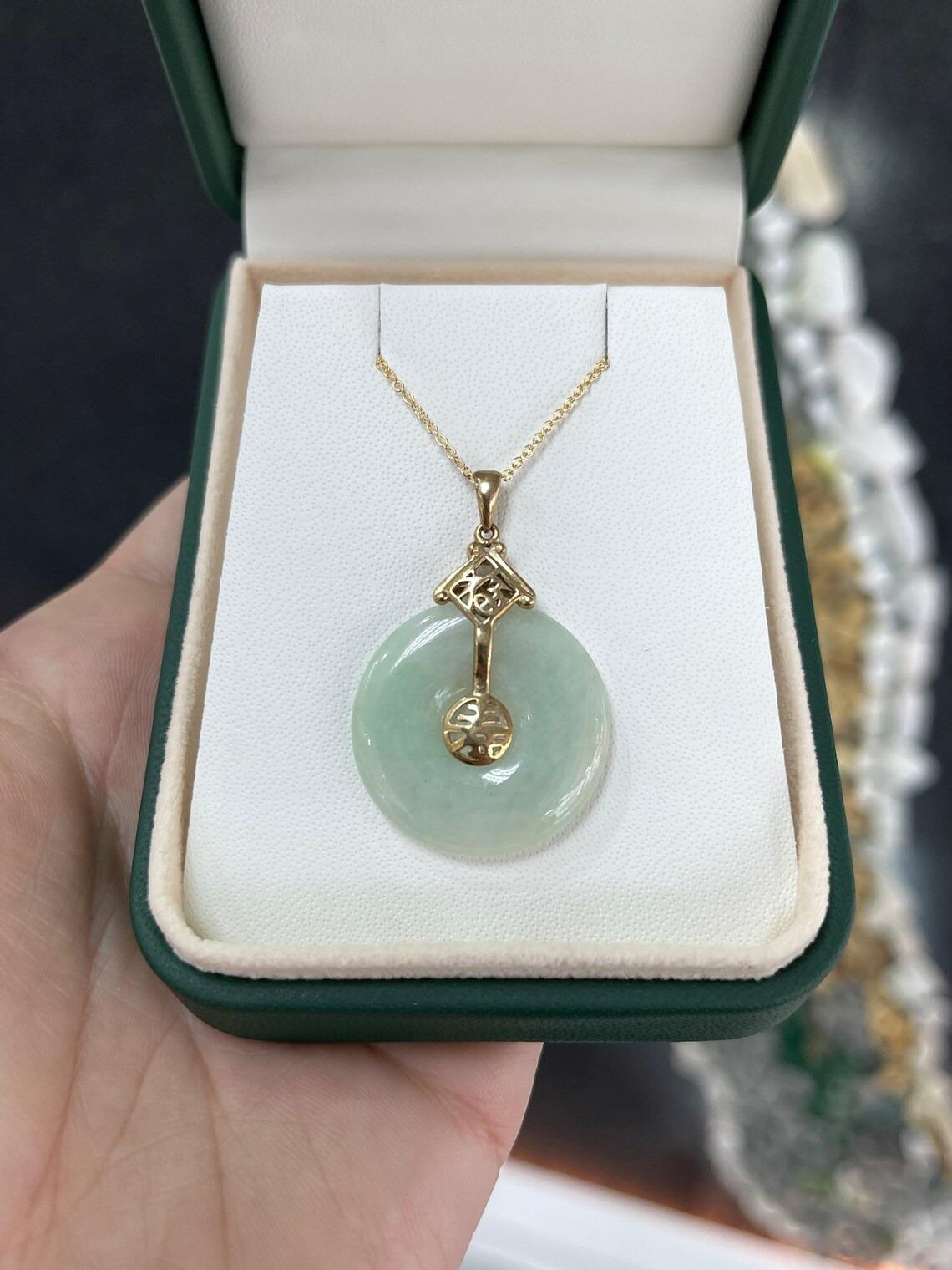 Displayed is a light green, natural jade, 10K gold medallion pendant. A custom-cut round jade is accented by Chinese letters in a simple and sophisticated design. 

*18