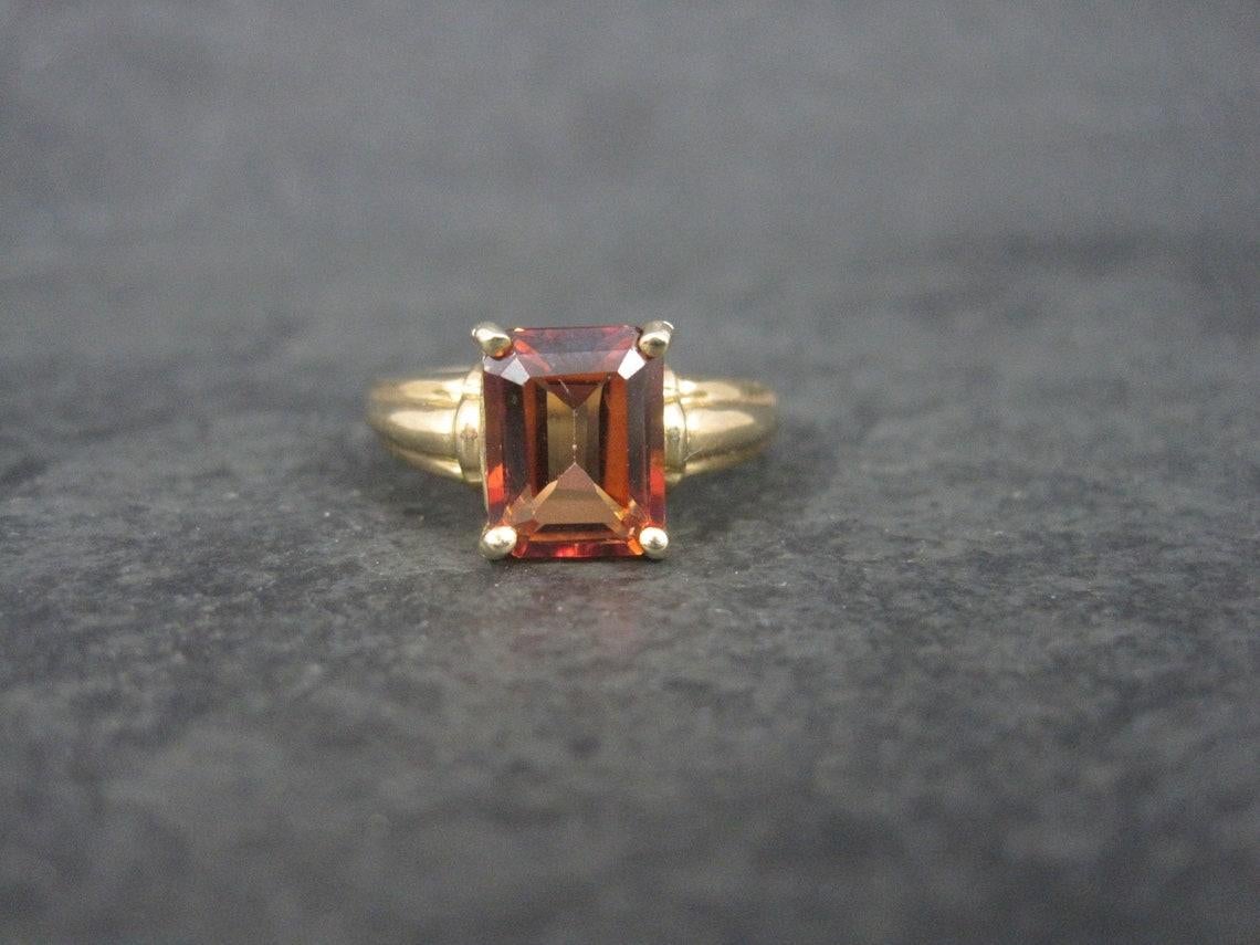 This gorgeous estate ring is 10k yellow gold.
It features a 3 carat, emerald cut reddish orange topaz gemstone.

The face of this ring measures 3/8 of an inch north to south.
Size: 6

Marks: 10K
