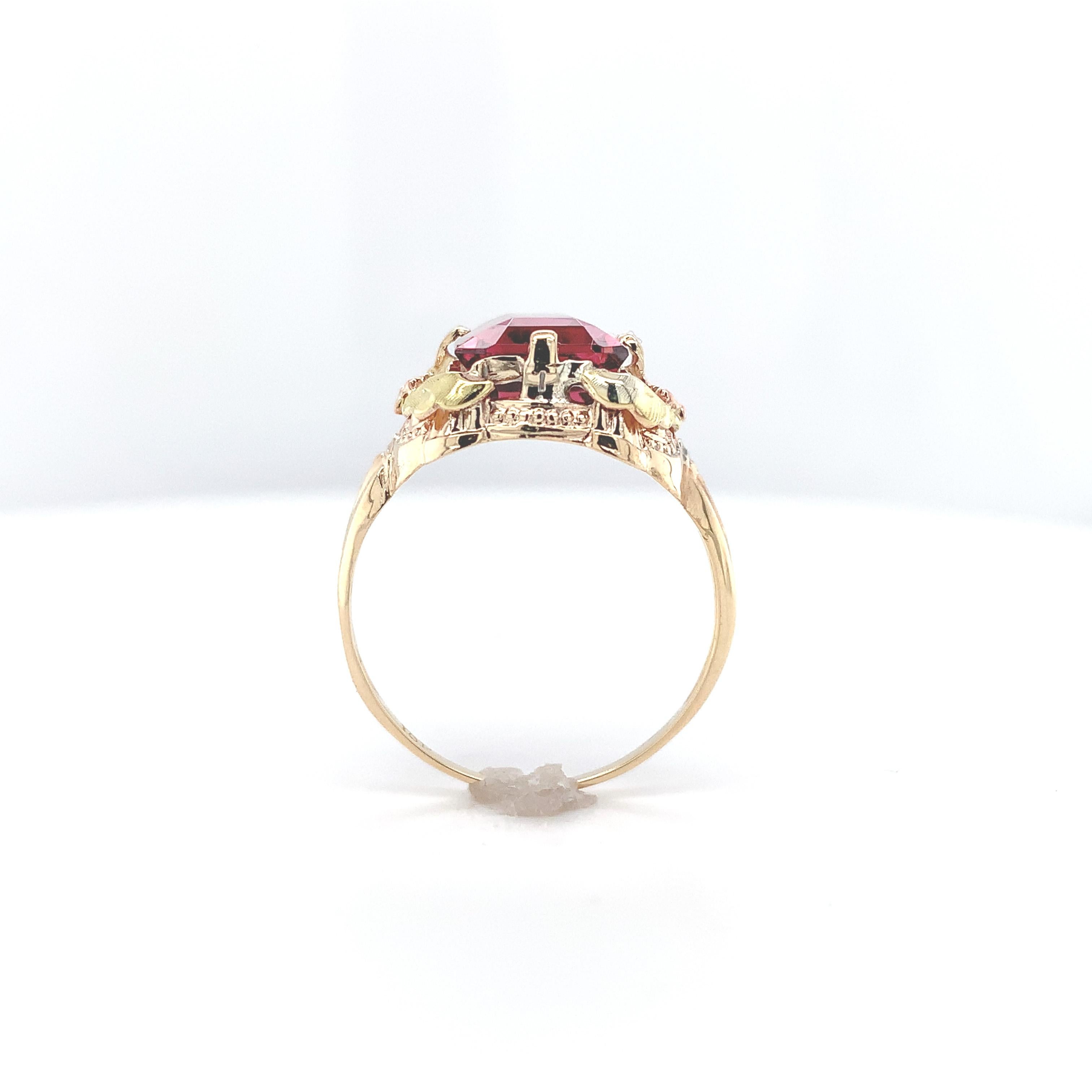 Vintage 10K gold filigree ring with applied rose gold flowers and green gold leaves featuring an emerald cut pink tourmaline. This beautiful orangy pink, pomegranate color tourmaline weighs 3.80 carats and measures about 10mm x 8mm. The ring fits a