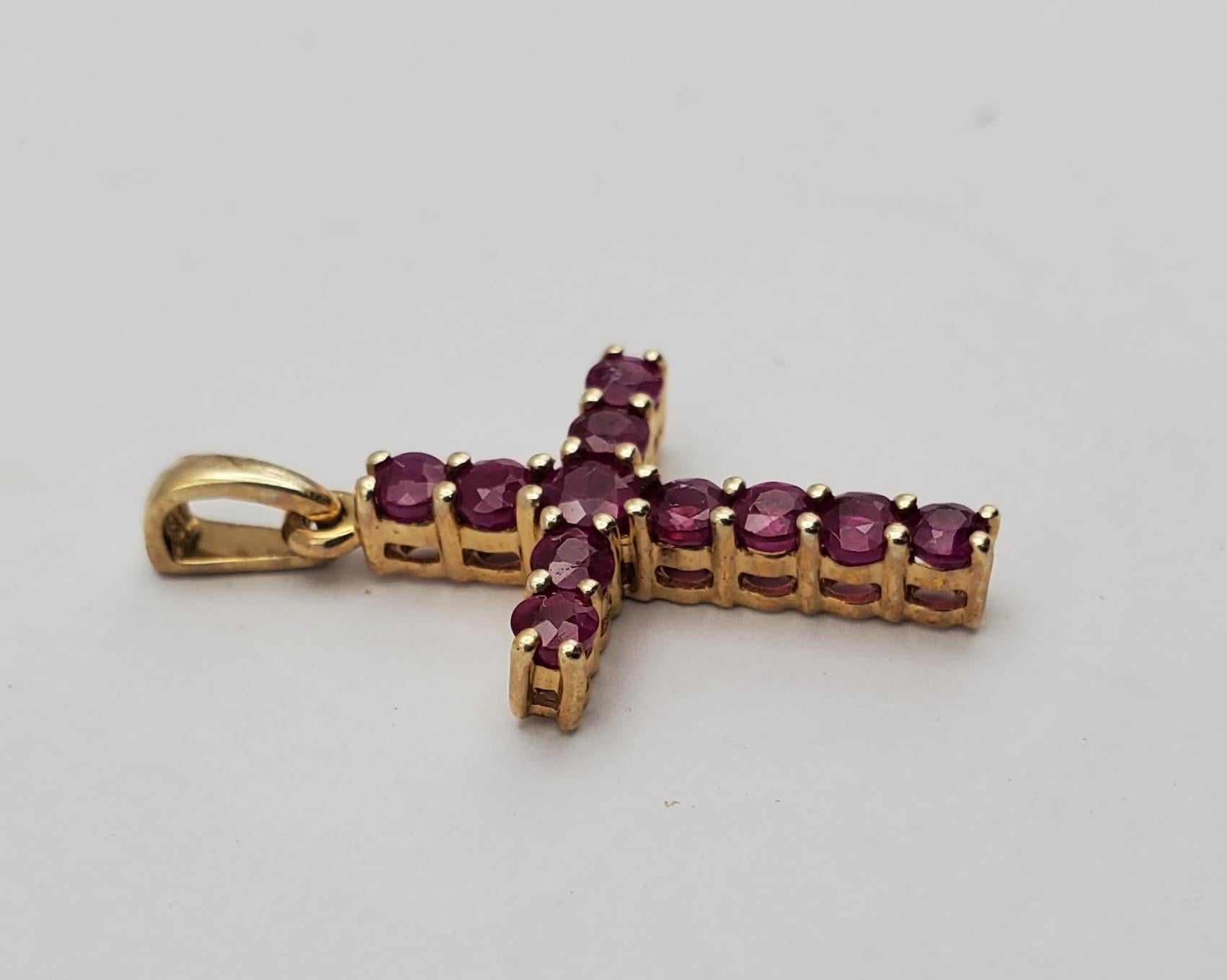 Precioso colgante en forma de cruz de oro amarillo de 10k y rubí natural. Esta cruz tiene 11 rubíes naturales redondos de talla brillante engastados en una montura sólida de cuatro garras compartidas. El cierre es un sólido estilo cónico que puede