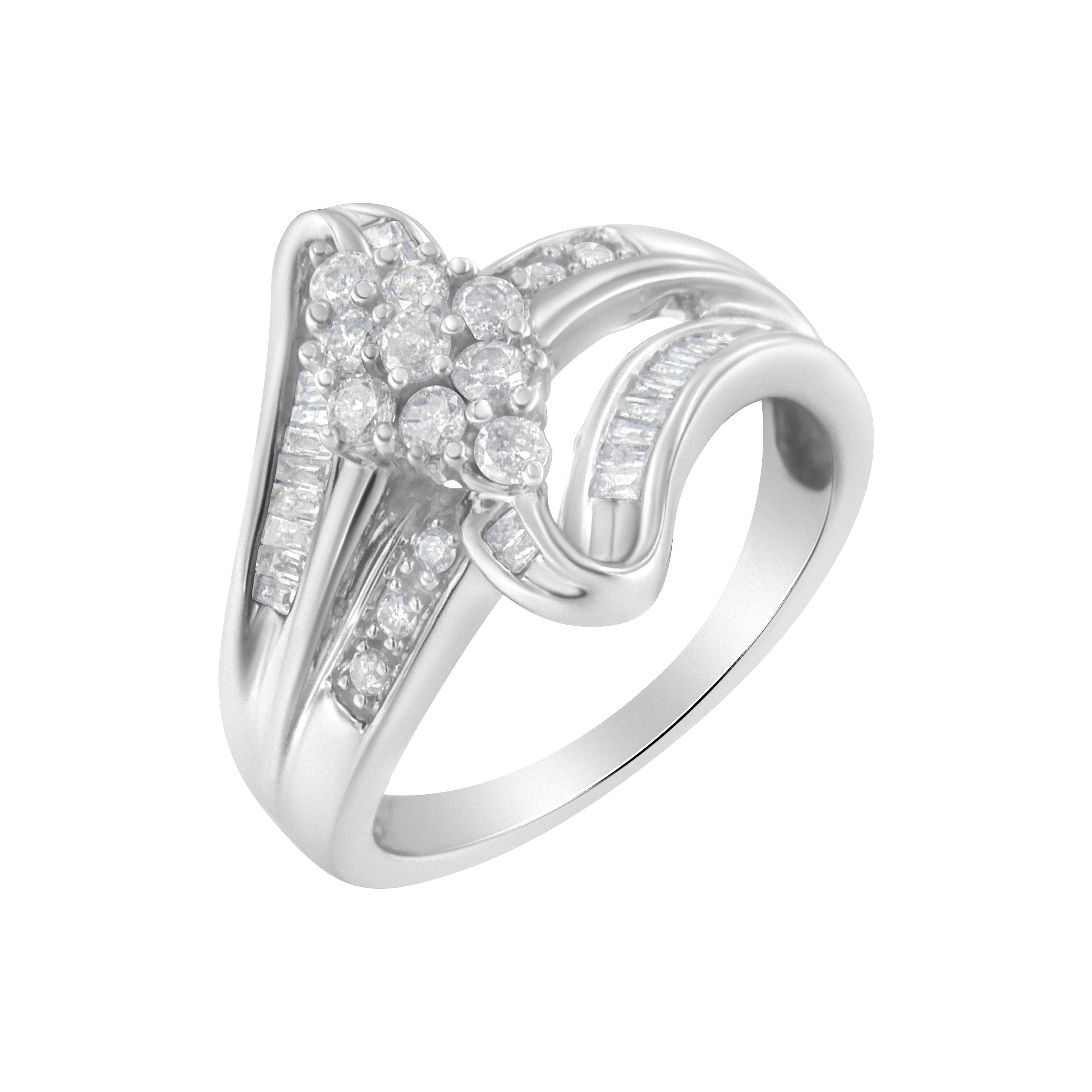 Realizzato in brillante oro bianco 10 carati, questo anello bypass mette in mostra uno splendido gruppo di diamanti rotondi. Morbidi nastri si separano dalla fascia dell'anello e circondano il grappolo. Diamanti rotondi e a baguette intarsiano i