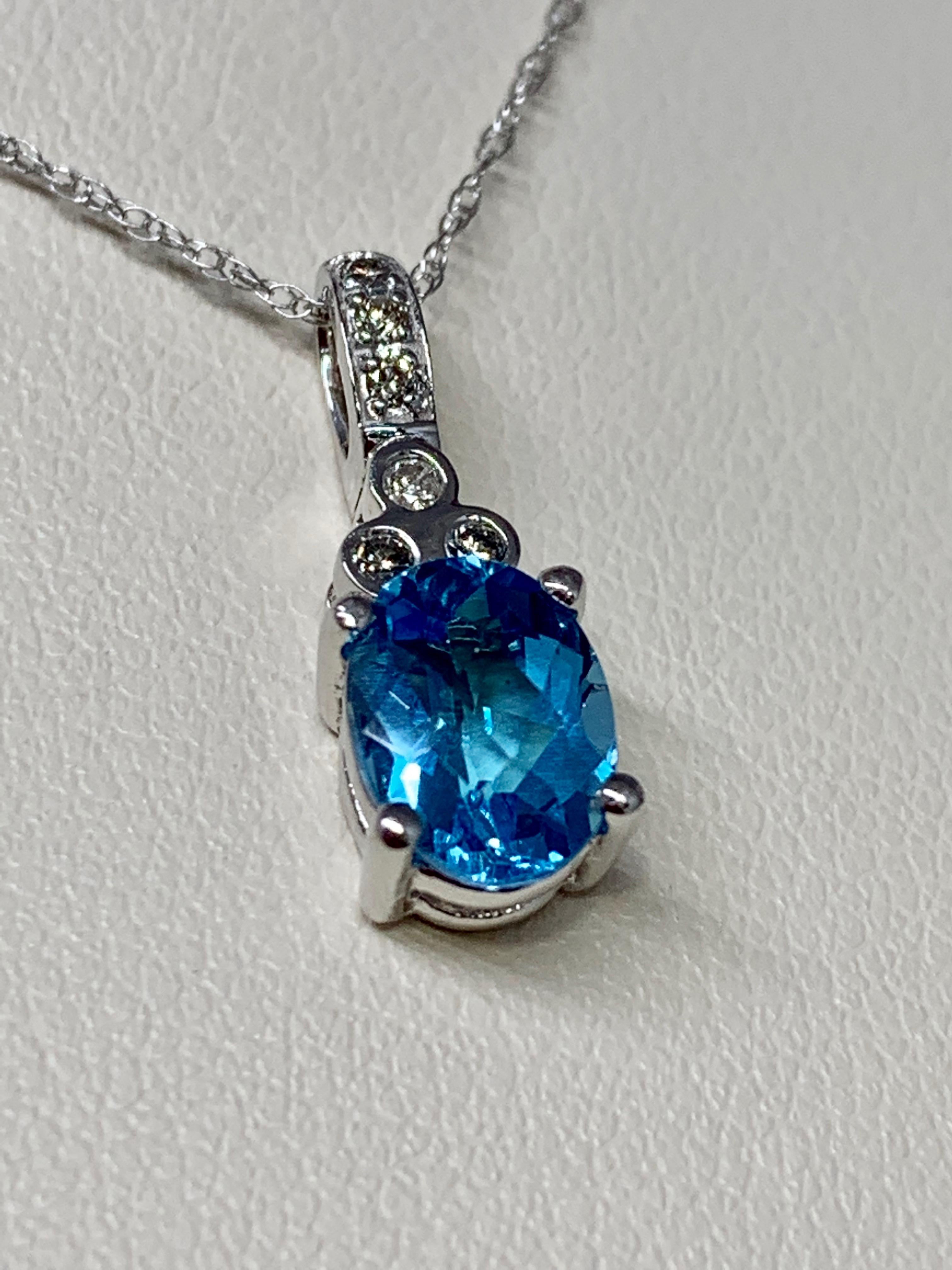 This beautiful pendant features a 1.25 carat oval-shaped blue topaz center stone with diamond accents weighing 0.07 carats. This pendant features round diamond bezel accents and a diamond bale. The mounting and 18 inch rope chain are both 10K white