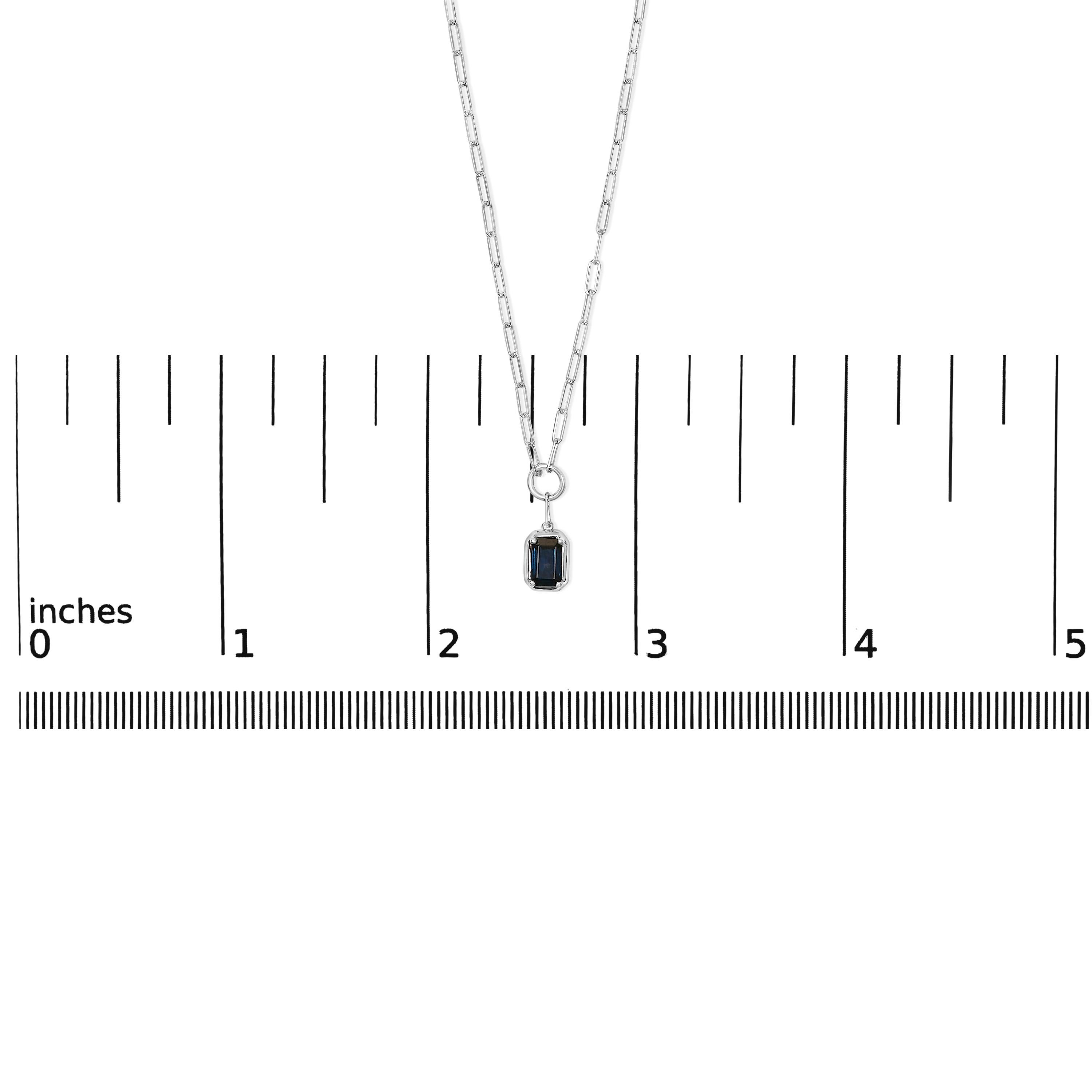 Eleg avec la profondeur sereine de l'océan, ce collier pendentif exquis rayonne d'une sophistication élégante. Fabriqué en or blanc 10 carats lustré et rhodié pour en rehausser l'éclat, il est orné d'un saphir bleu taillé en émeraude. Cette pierre