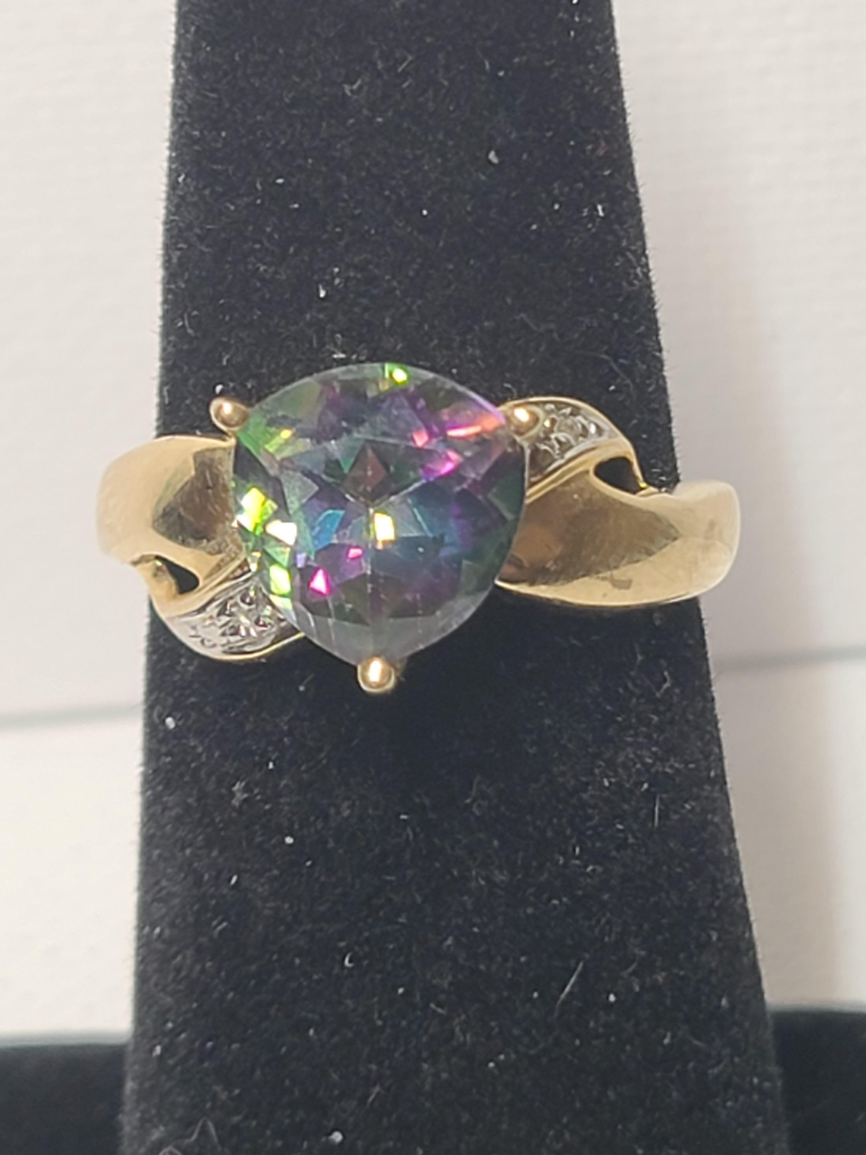 This estate found ring features a trillion cut mystic topaz that measures 9x8.5mm with shoulder set accent diamonds. The three prong setting is 10K yellow gold and weighs 2.6 grams. 
The ring size is 6.5 (US).