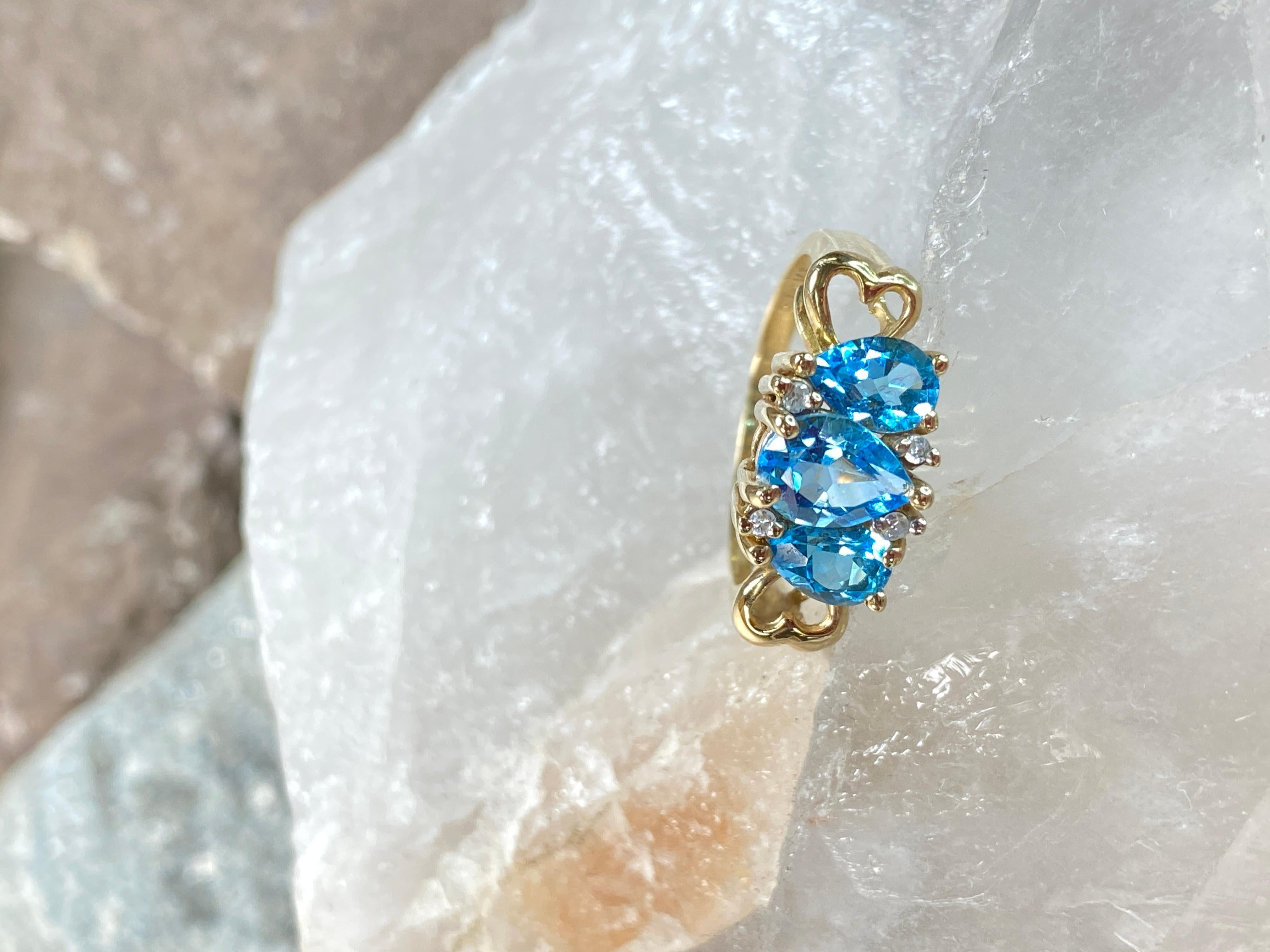 This anniversary ring is a breathtaking testament to enduring love, crafted in lustrous 10K yellow gold. At its center sits a mesmerizing pear-shaped Swiss blue topaz, evoking the serene depths of the ocean with its captivating azure hue. Flanked on