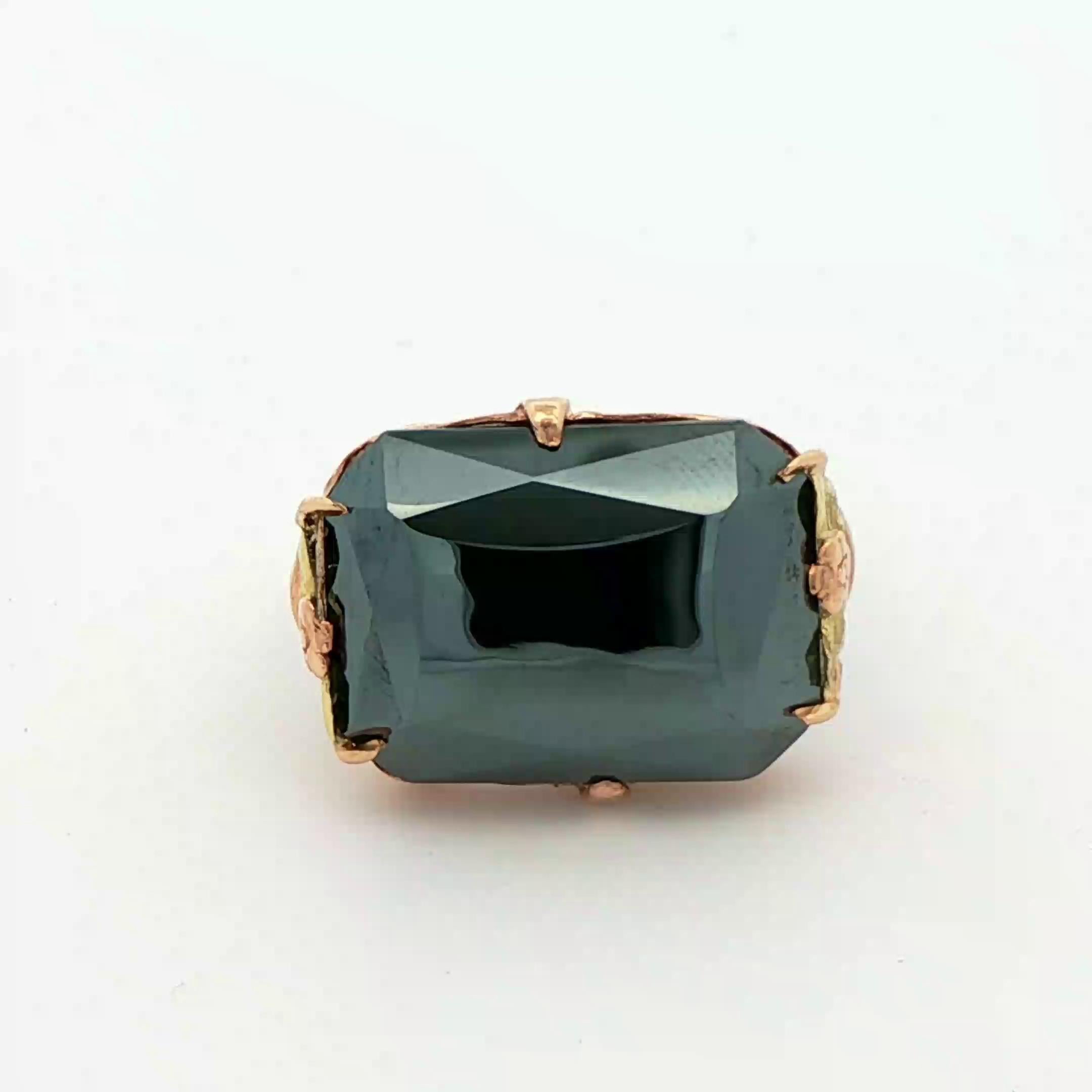 Este precioso anillo Art Decó de hematites procede de los años 20 y se fabricó con oro amarillo y verde de 10 quilates. El anillo presenta una hematites negra natural, de corte rectangular, con un brillo de espejo. La hematites está engastada en una
