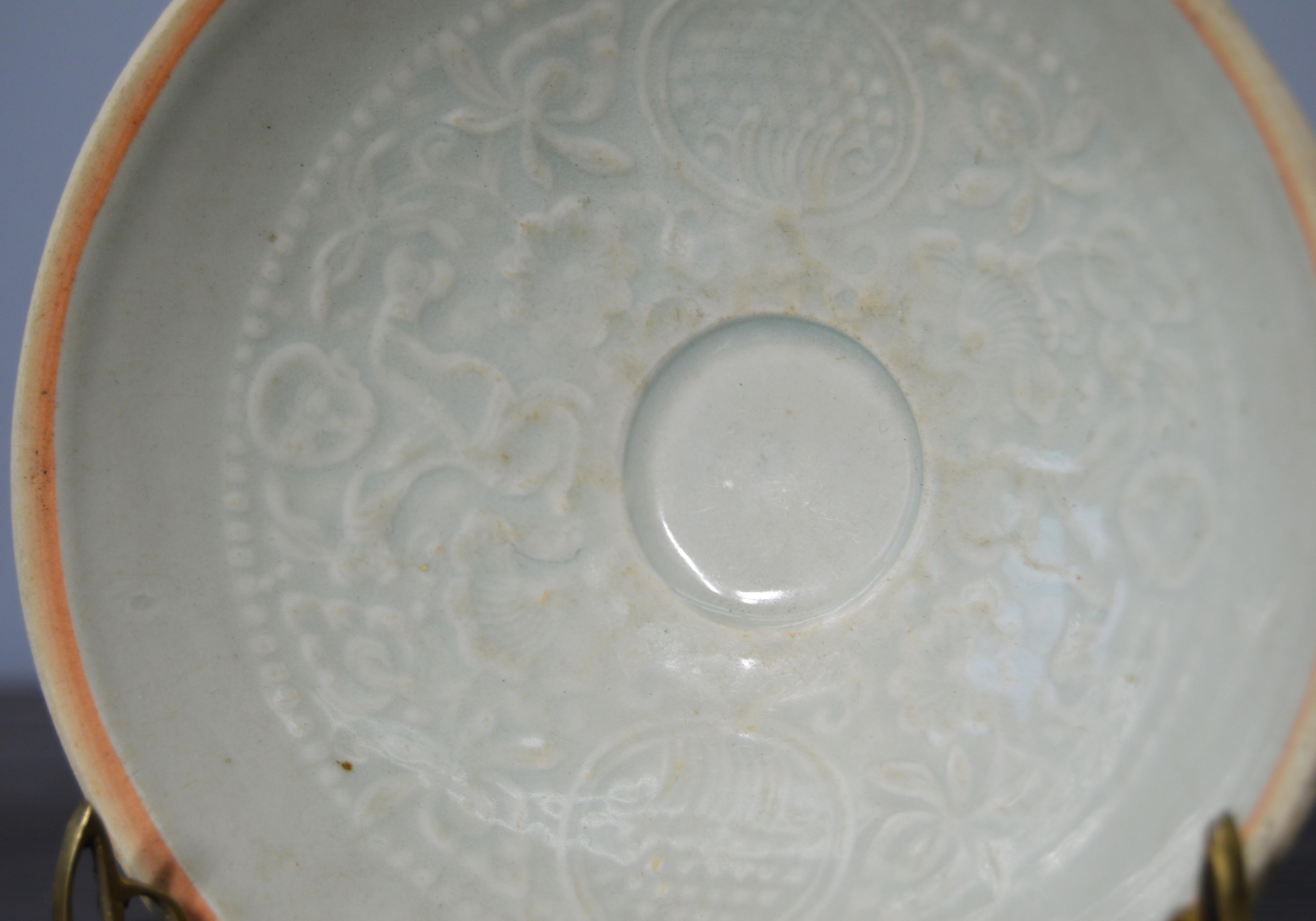 This antique Chinese bowl with intricate motifs was made from celadon porcelain during the Song dynasty: 960–1279. This small Chinese circular bowl adopts a elegant almost conic shape raised on a circular base. The piece displays a pale celadon