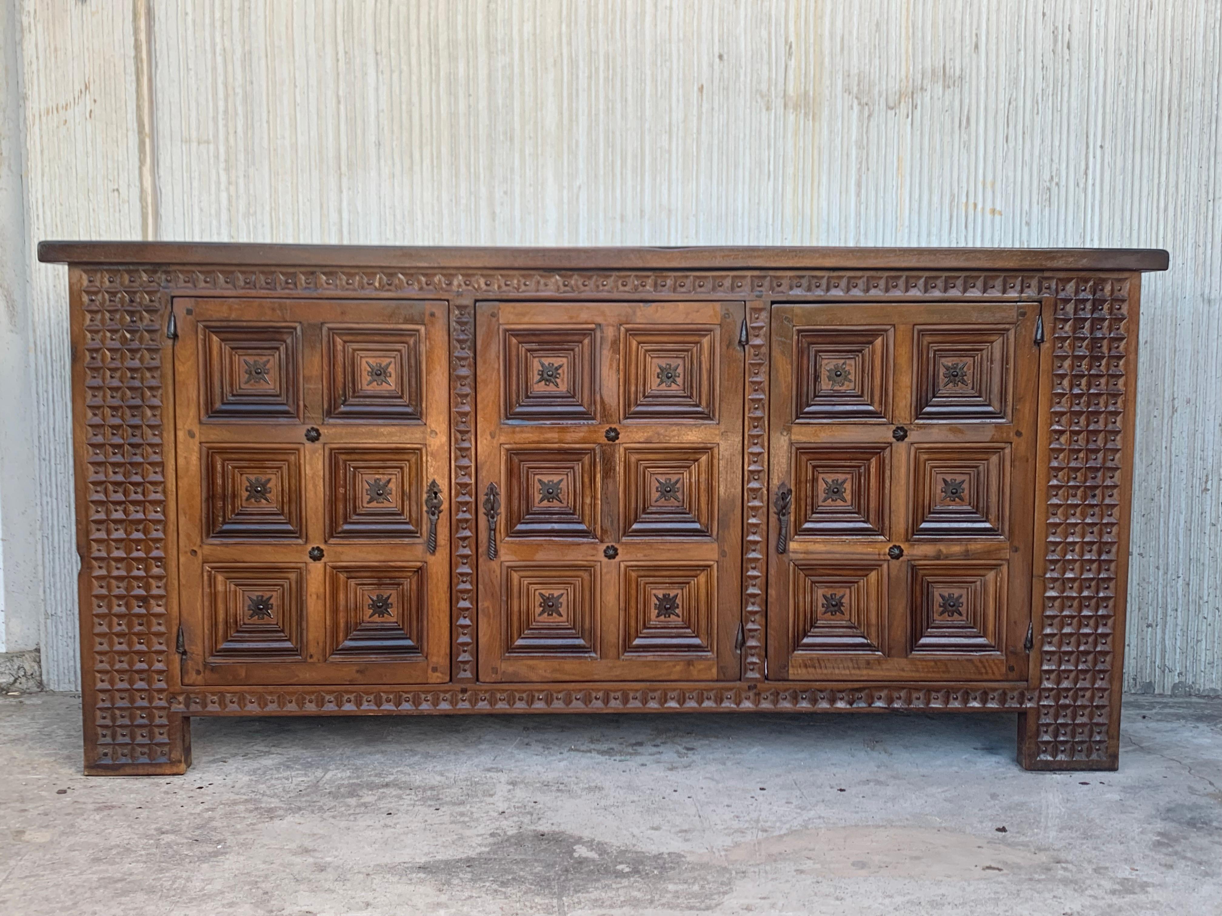 From Northern Spain, constructed of solid walnut, the rectangular top with molded edge atop a conforming case housing three doors, the doors paneled with solid walnut, raised on a plinth base. The doors are hand carved in the edges of the pieces.