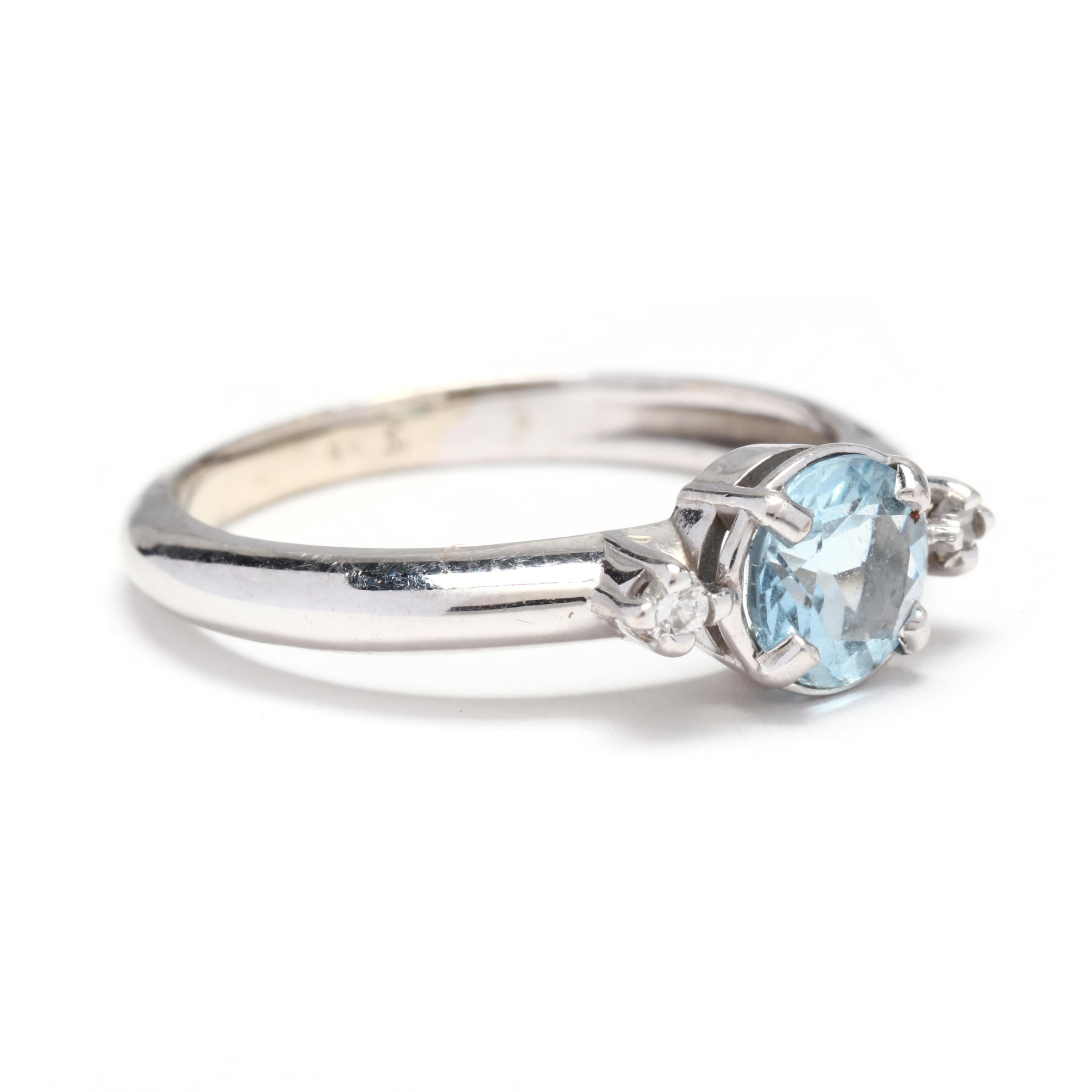 A 10 karat white gold blue topaz and diamond ring. This ring features a prong set, round cut blue topaz center stone weighing approximately .60 carat with a full cut round diamond on either side weighing approximately .02 total carats and a thin,