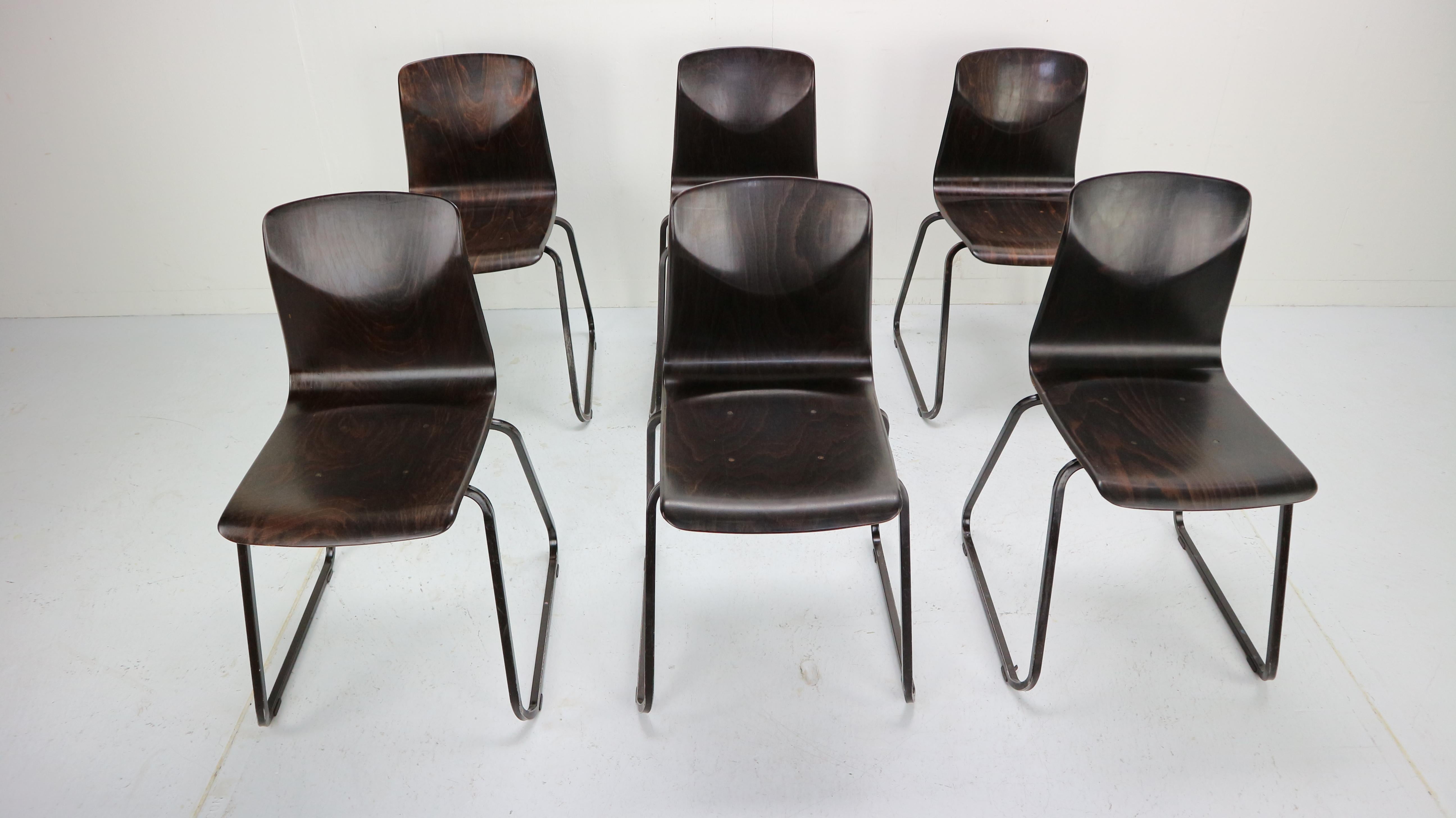 Thur-op-seat chairs with stackable metal frame. This industrial school or dining room chairs are made at Galvanitas, Holland (see logo G) in 1970's.
They were created because of a partnership between Galvanitas and Pagholz, (West Germany). The base