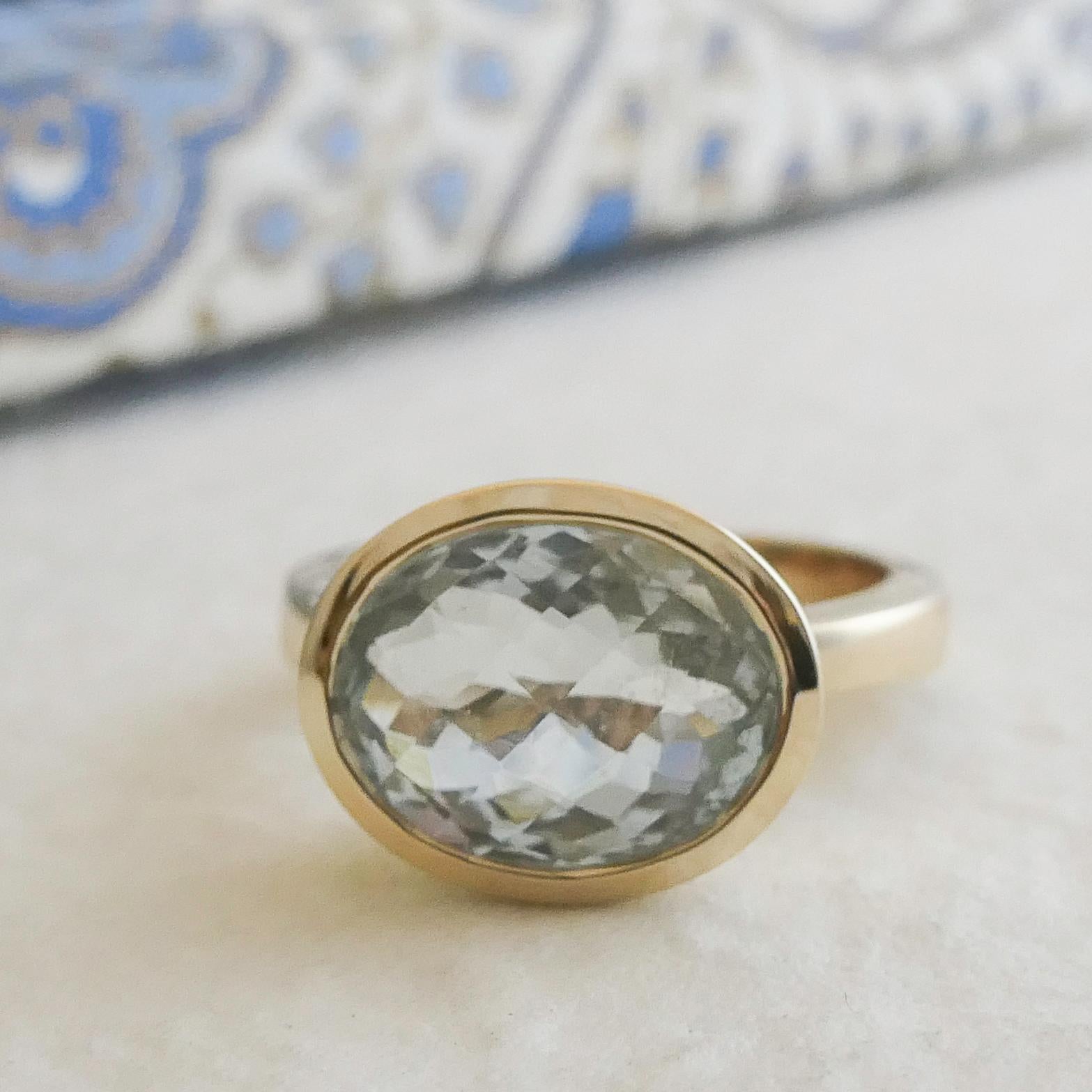 Cette élégante bague est ornée d'une aigue-marine ovale à facettes de 10 x 12 mm, sertie dans un élégant chaton en or jaune 14 carats. La teinte bleue pâle et douce de l'aigue-marine contraste magnifiquement avec les tons chauds et dorés, créant un