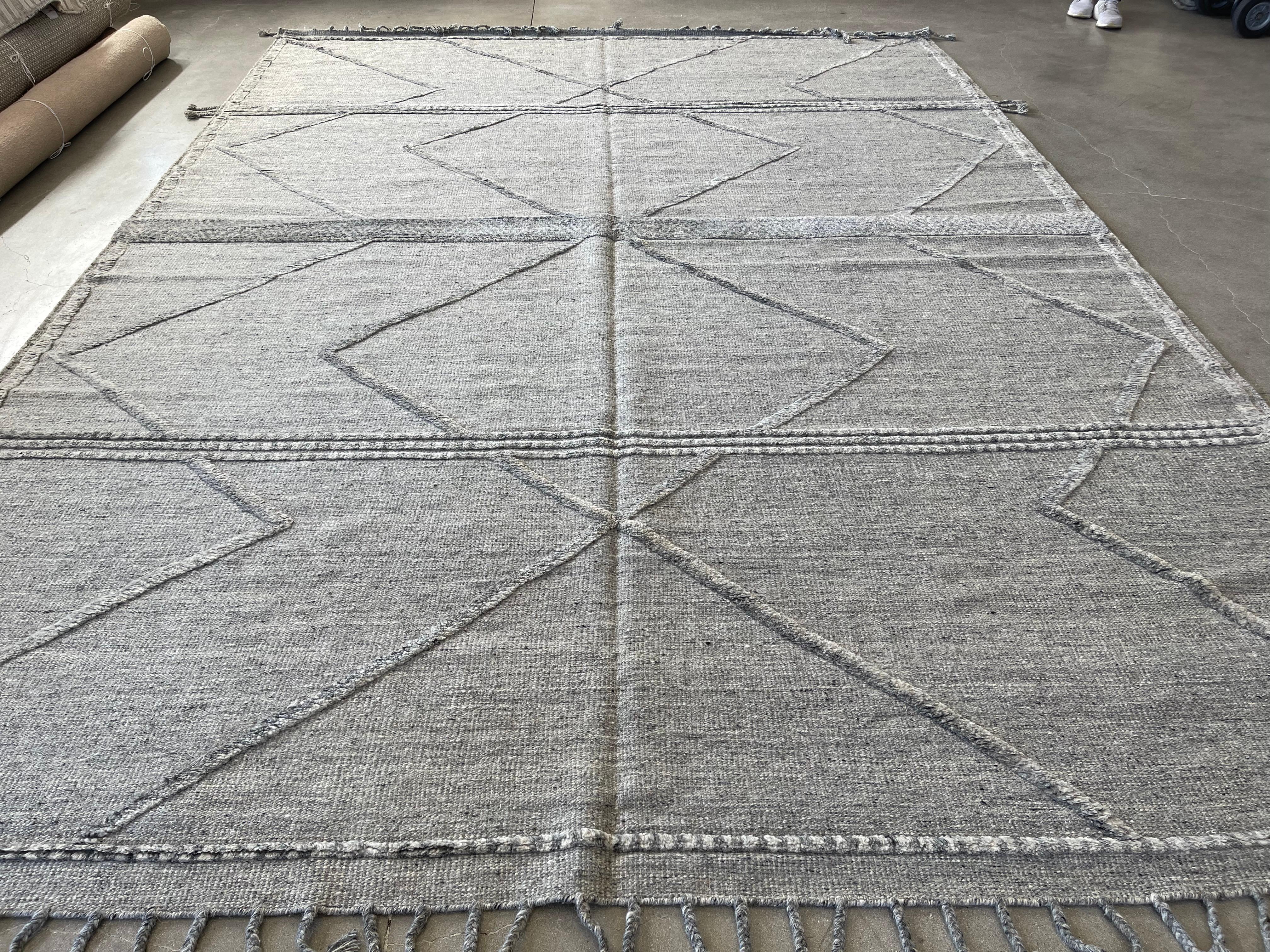 Rehaussez votre espace avec notre tapis 10'x14' en laine nouée à la main en Inde, au design marocain gris sourd. Doté d'un superbe design de transition, ce tapis ajoute du style et un confort luxueux à n'importe quelle pièce. Fabriqué en laine de