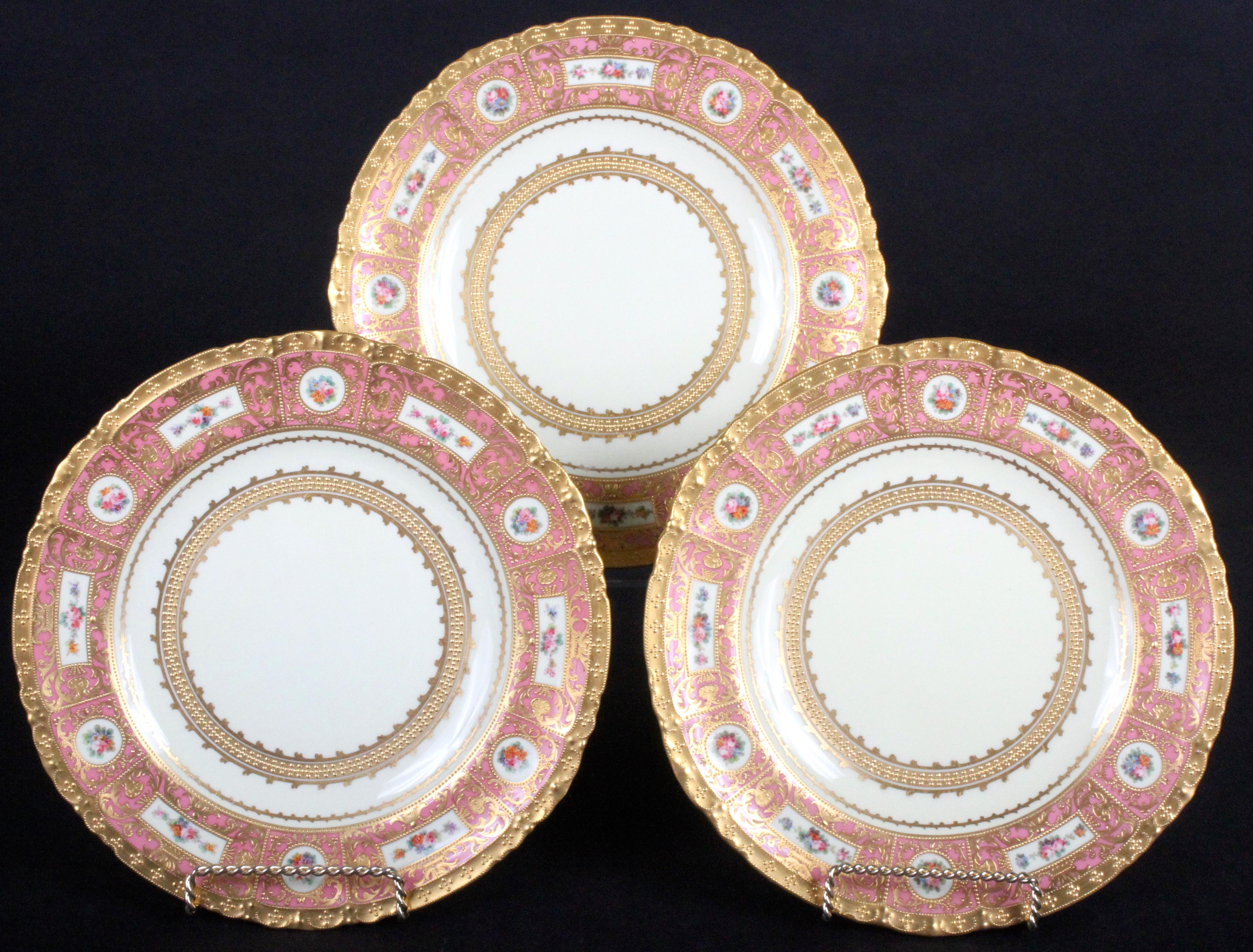 These 11 ornate service or dinner plates are from the esteemed Royal Crown Derby firm of Derby, England. The plate rim is divided into 6 rectangular panels that feature hand painted groups of flowers, the rectangular panels are separated by 6
