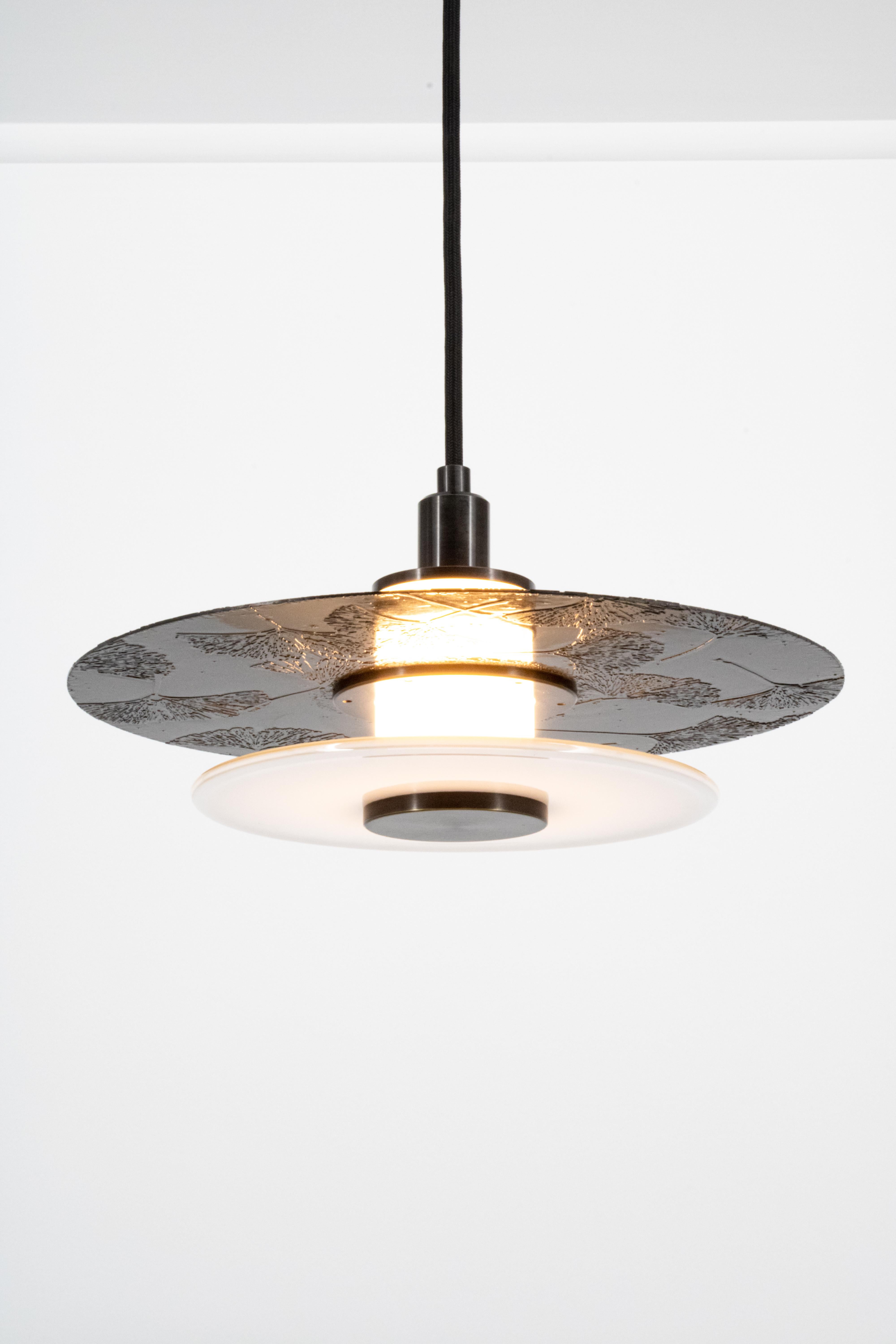 At eleven inches in diameter the Klein Pendant embraces a layered light assembly comprising a hand blown glass rondelle and an etched and polished brass disc. Mounted to a central white light tube, the Klein Pendant offers ample up lighting as well